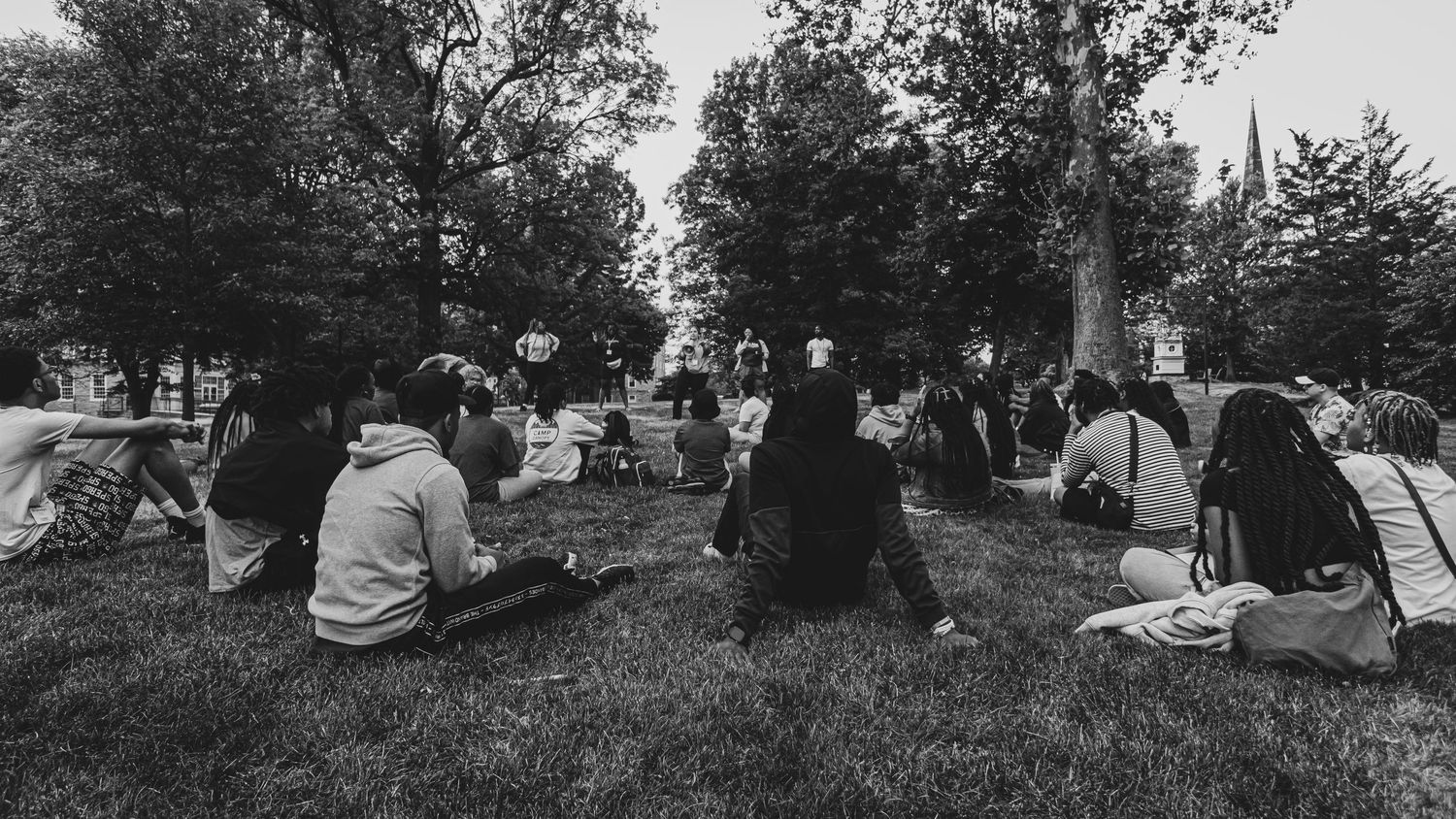 Black and white image of people relaxing on grass under trees.