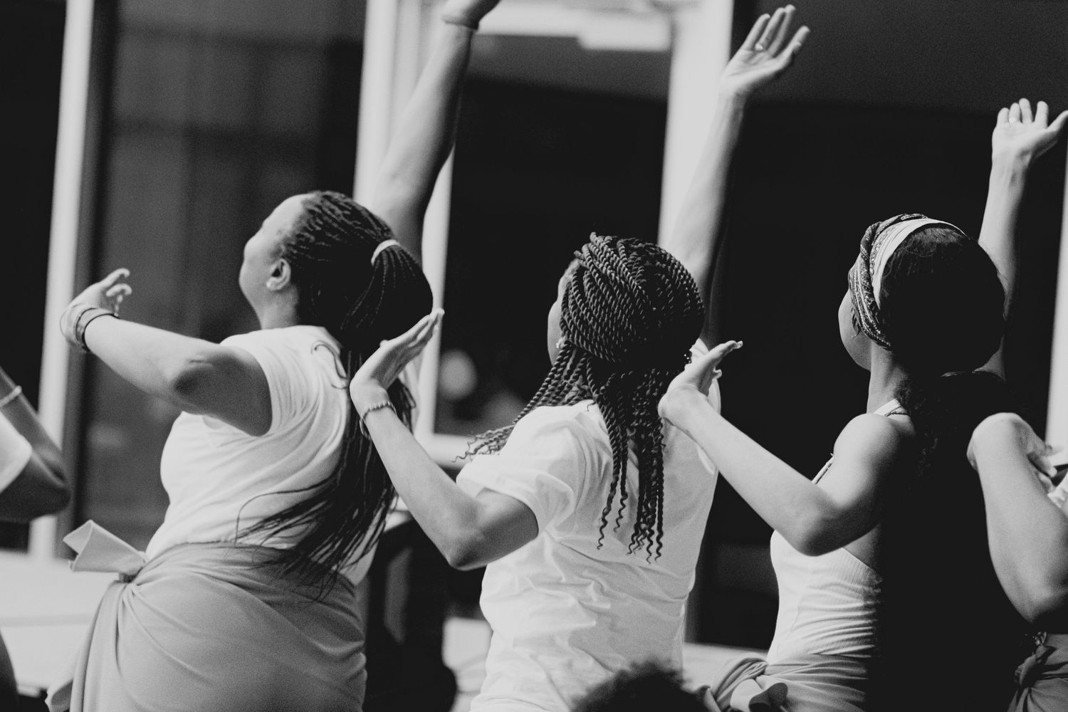 Three figures in white raising their arms in synchronized dance movement.