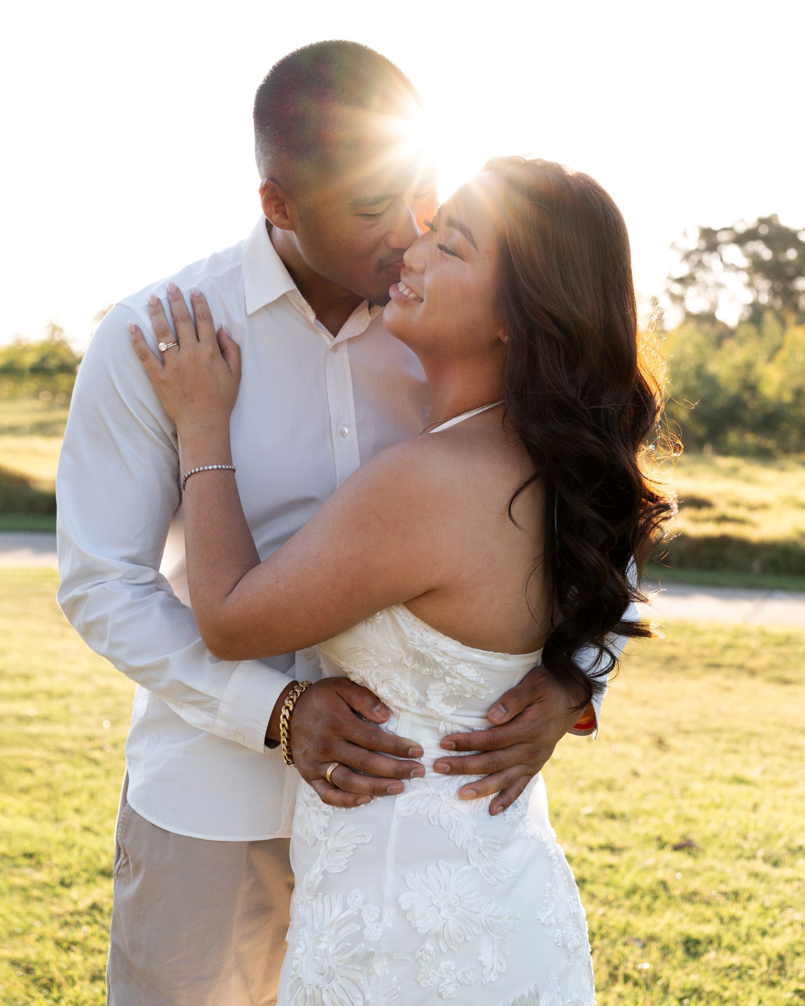 Golden sunlight illuminates a romantic moment between a couple in white against a natural backdrop.