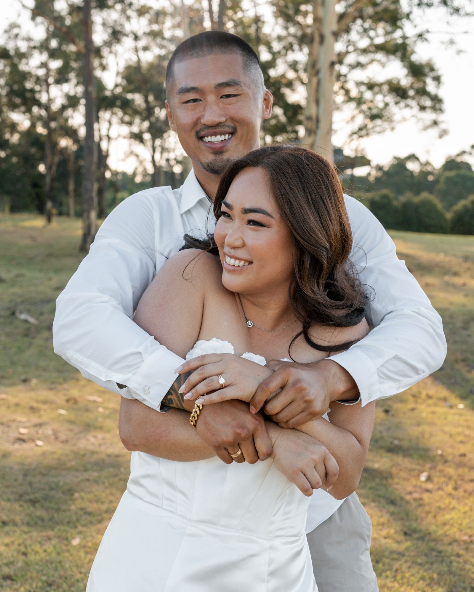 A candid moment of laughter and joy captured between a couple in white clothing outdoors.
