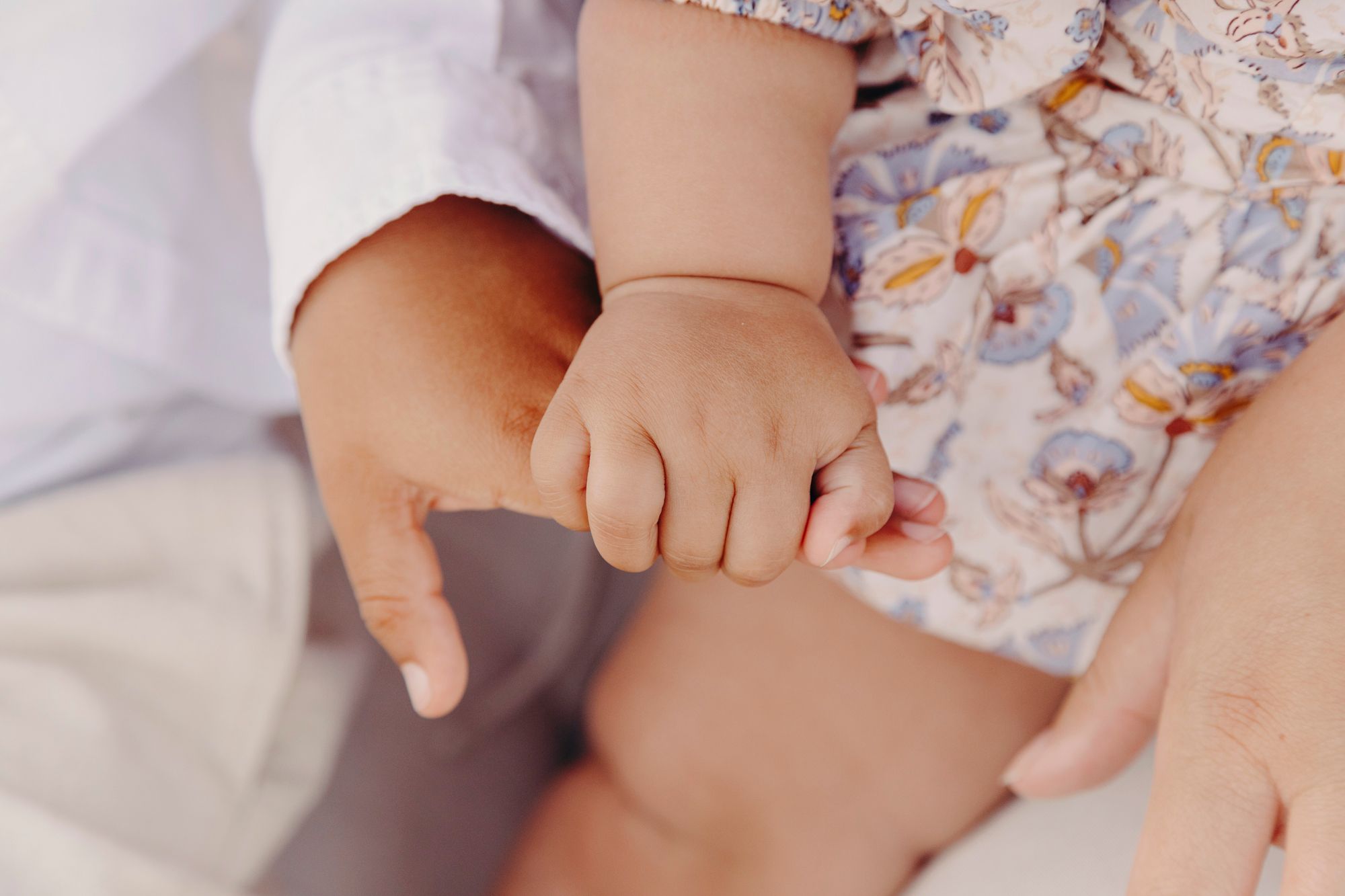 Close-up view of a baby's small hands resting on soft floral fabric and white bedding.