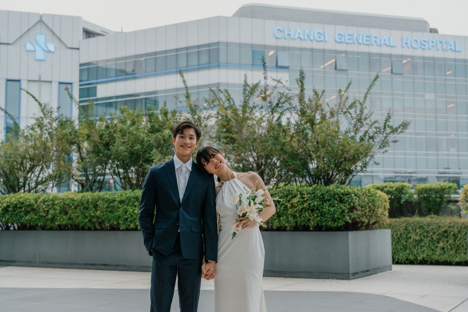 Newlyweds pose together against modern glass building exterior.