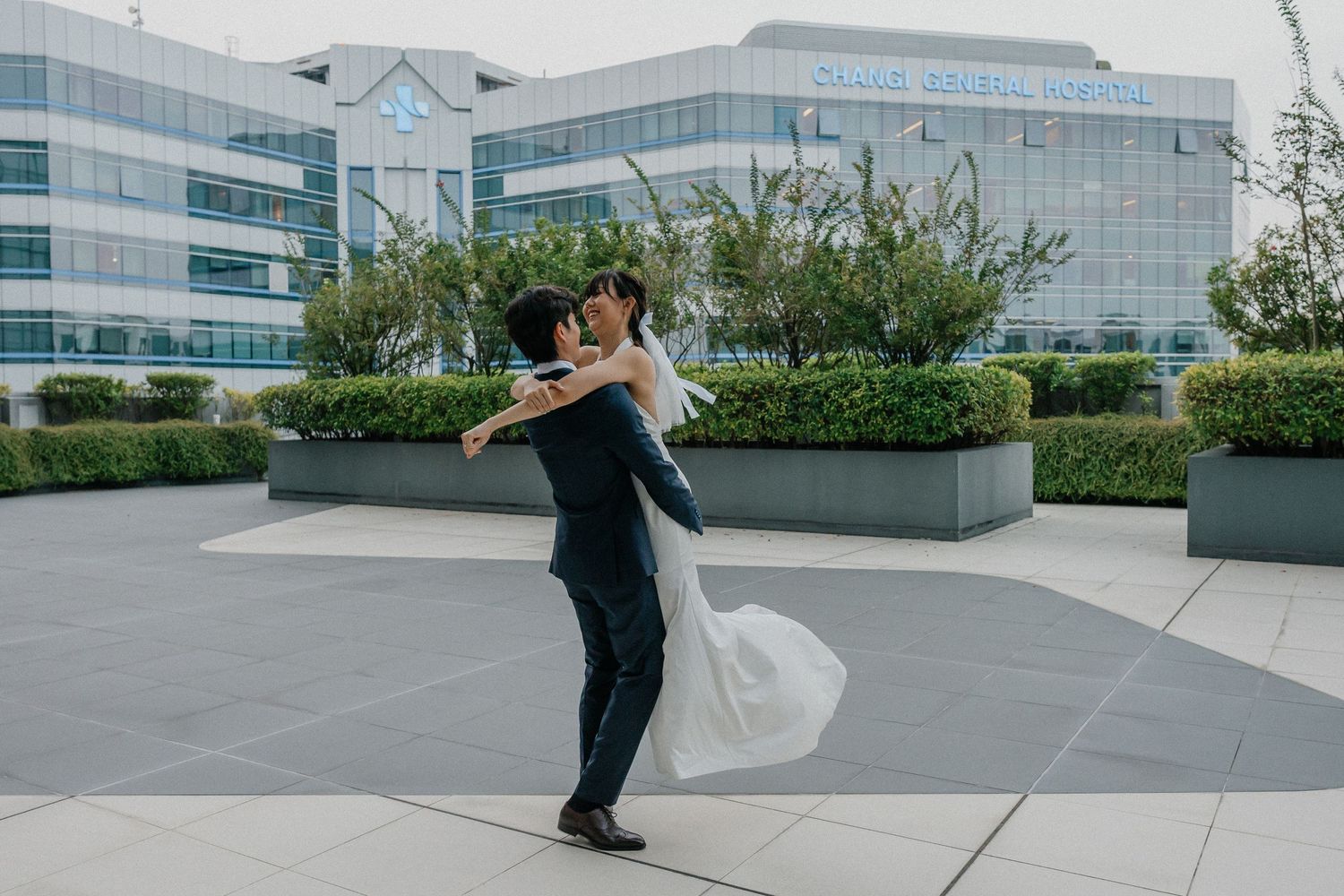 Groom lifts and spins bride in white dress on outdoor terrace.