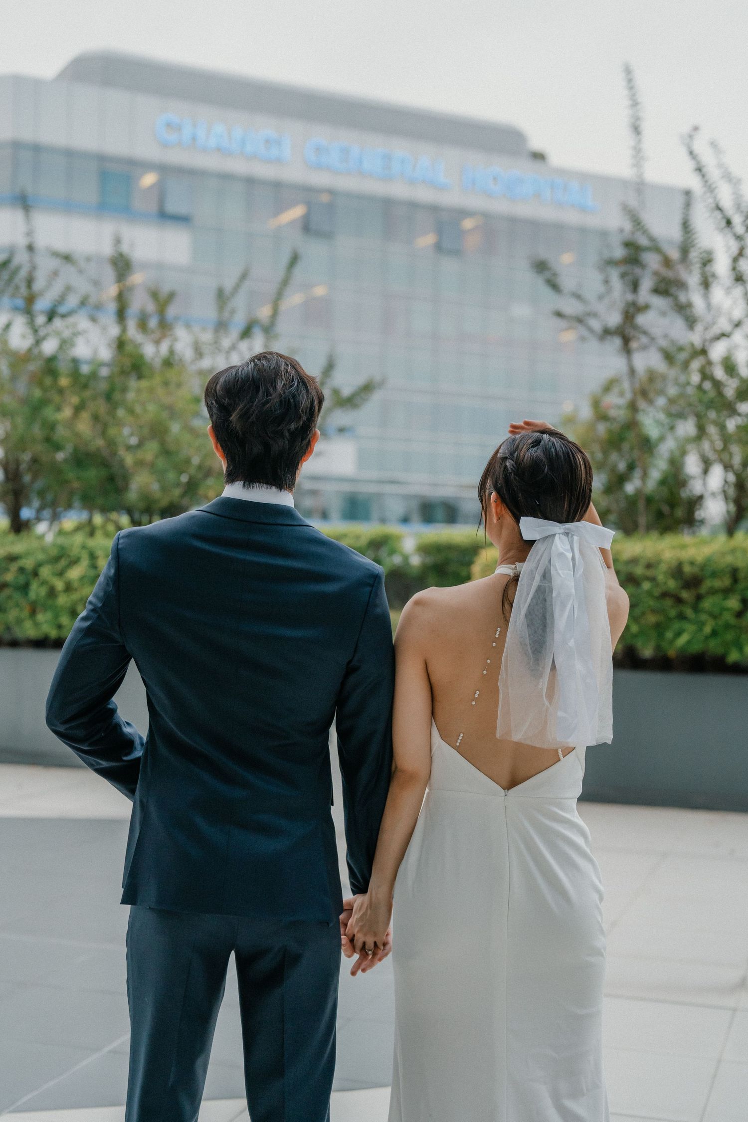 Back view of couple holding hands facing modern building with glass facade.