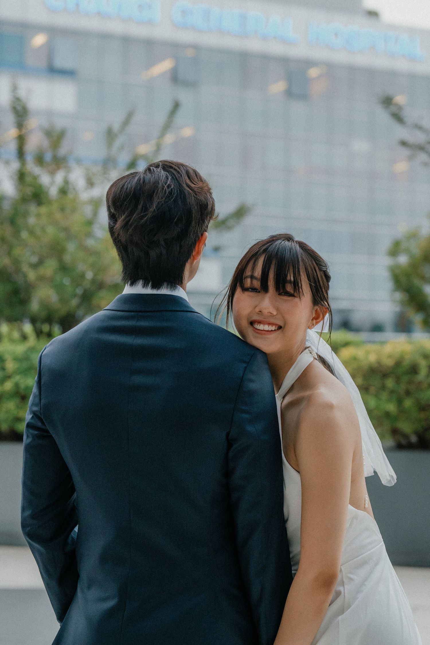 A joyful wedding portrait taken outside a medical facility with modern architecture.
