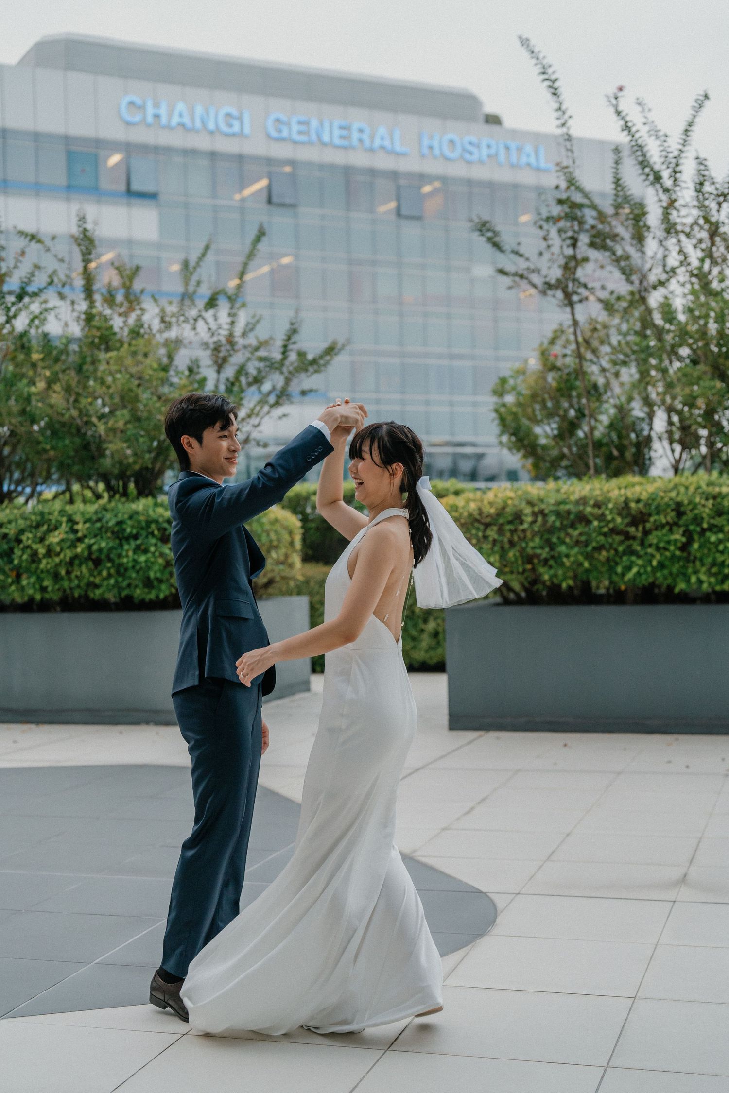 A playful wedding dance pose captured outside Changi General Hospital on a bright day.
