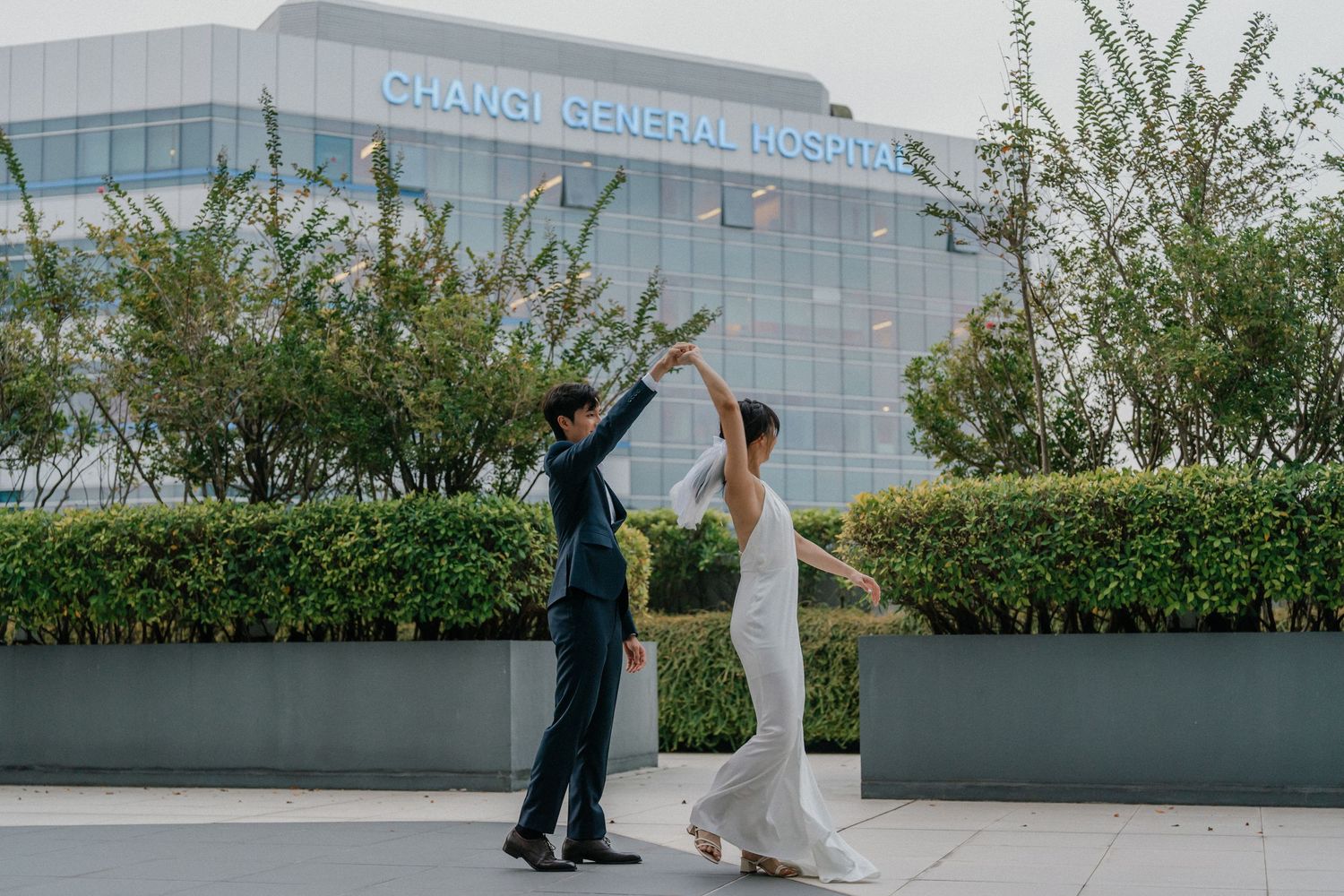 A lighthearted wedding moment with dancing and laughter outside a modern hospital.