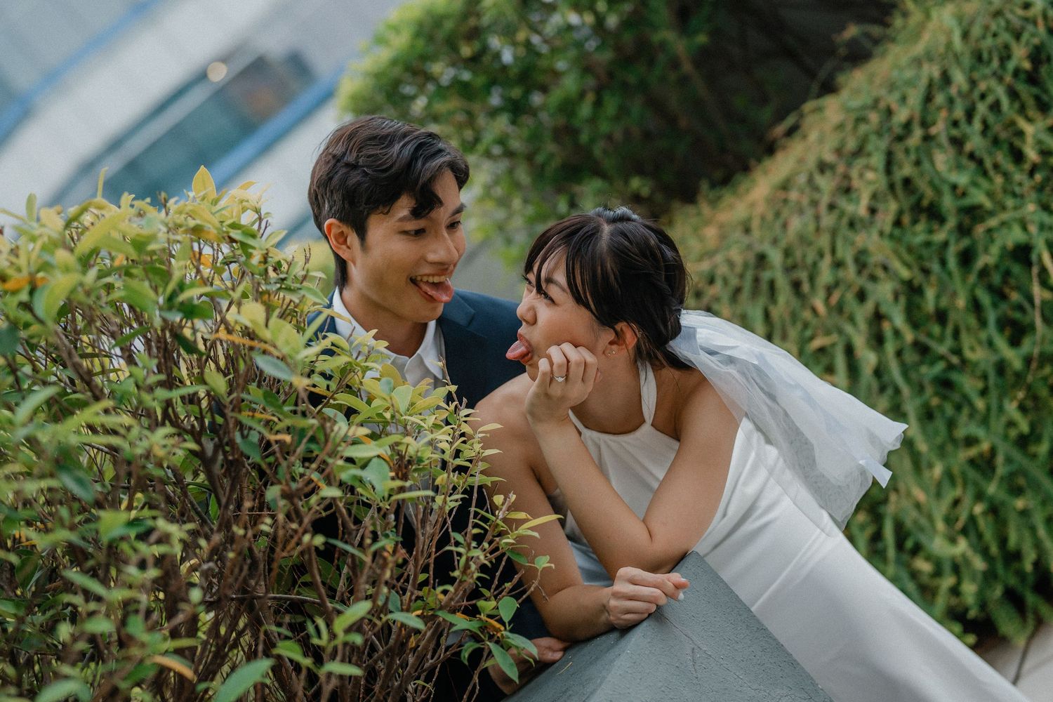 An intimate wedding portrait amongst the greenery outside a modern building.
