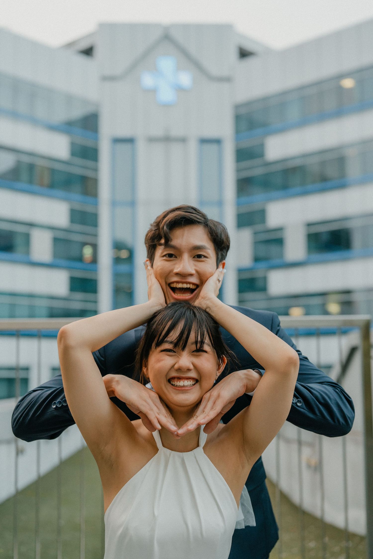 A playful couple poses for a fun portrait in front of a modern white building.