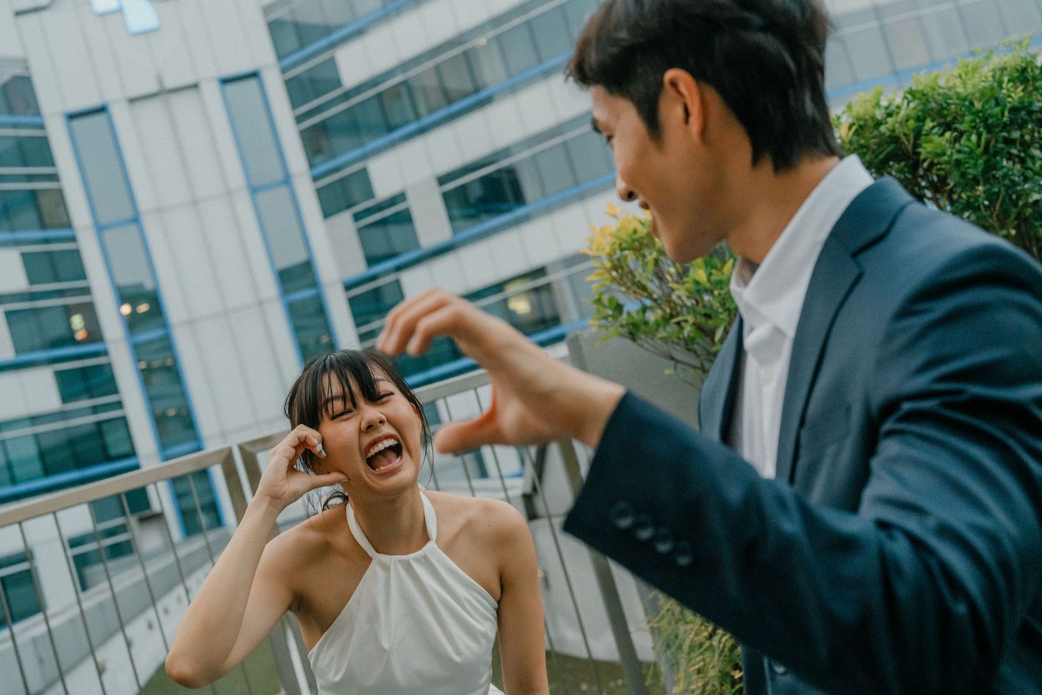 A couple shares a lighthearted moment making hand gestures together outdoors.