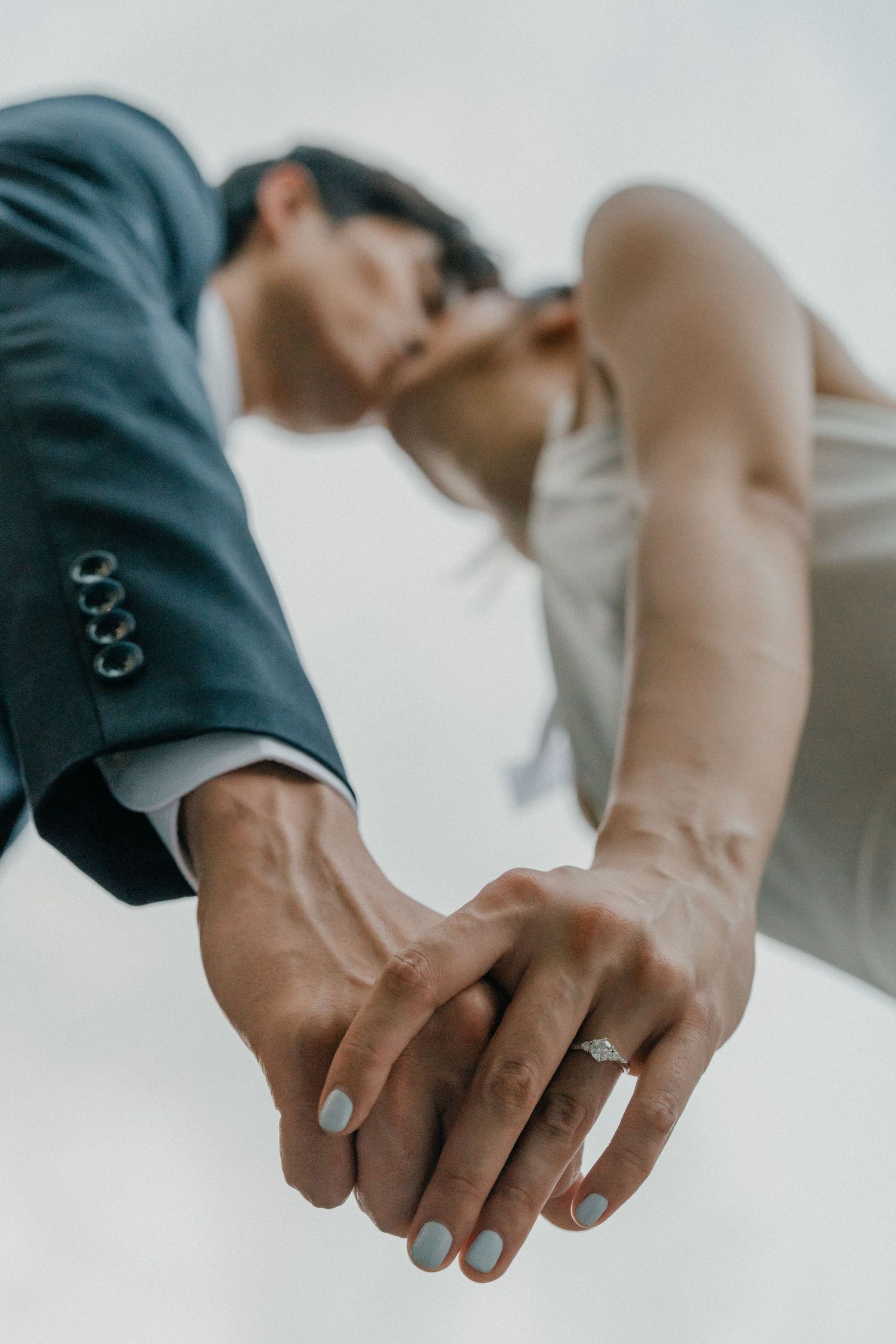 Close-up shot of joined hands showing an engagement ring against formal wedding attire.