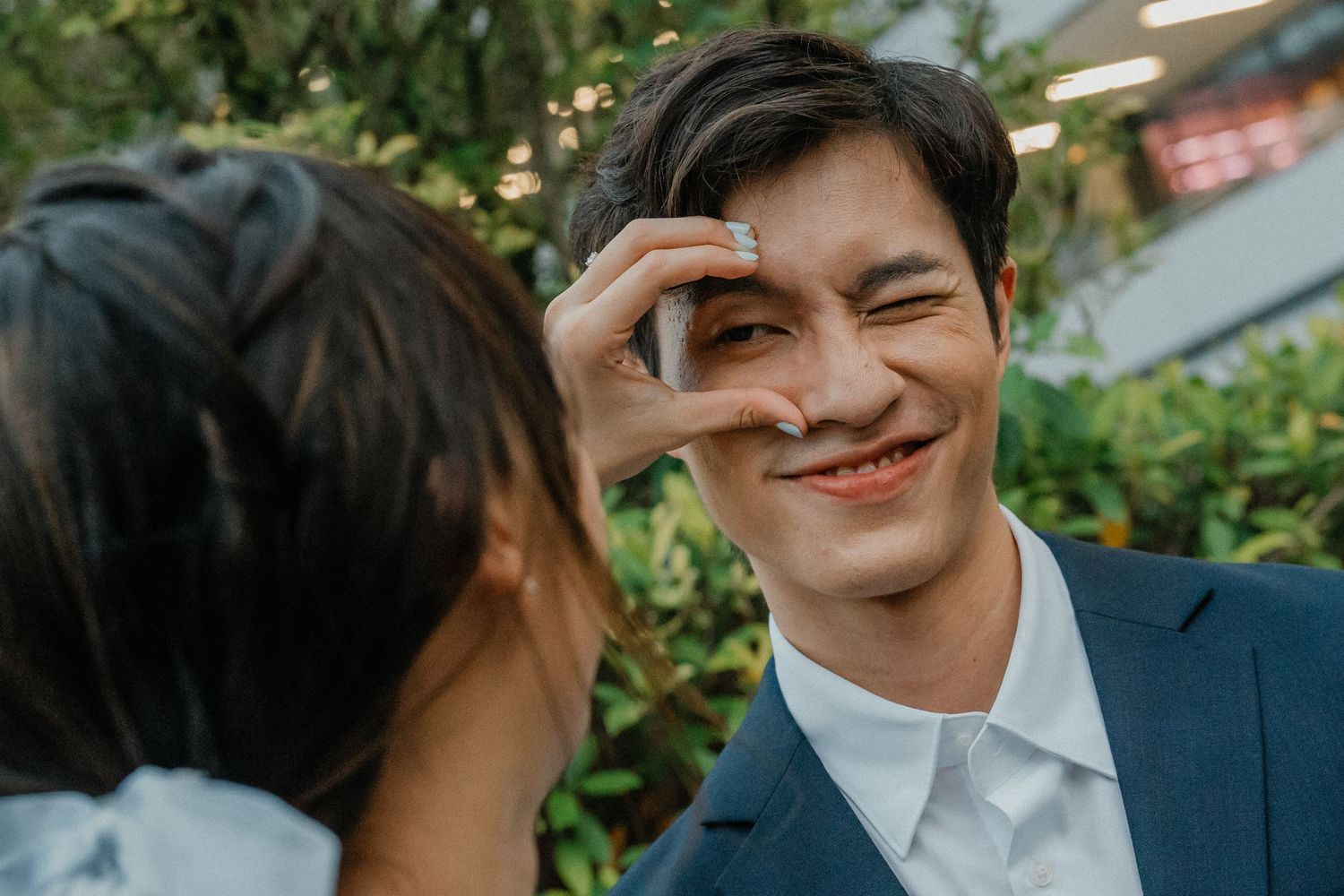 A couple shares a romantic moment making a heart shape with their hands among greenery.