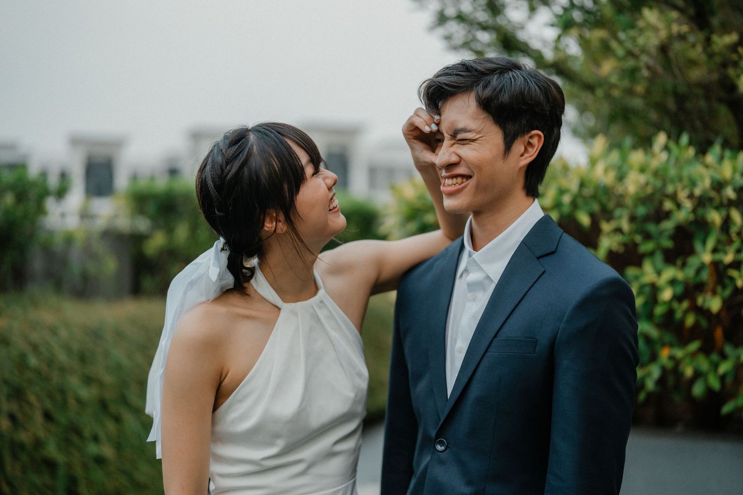 A couple in formal attire shares an intimate moment together against a backdrop of green foliage.