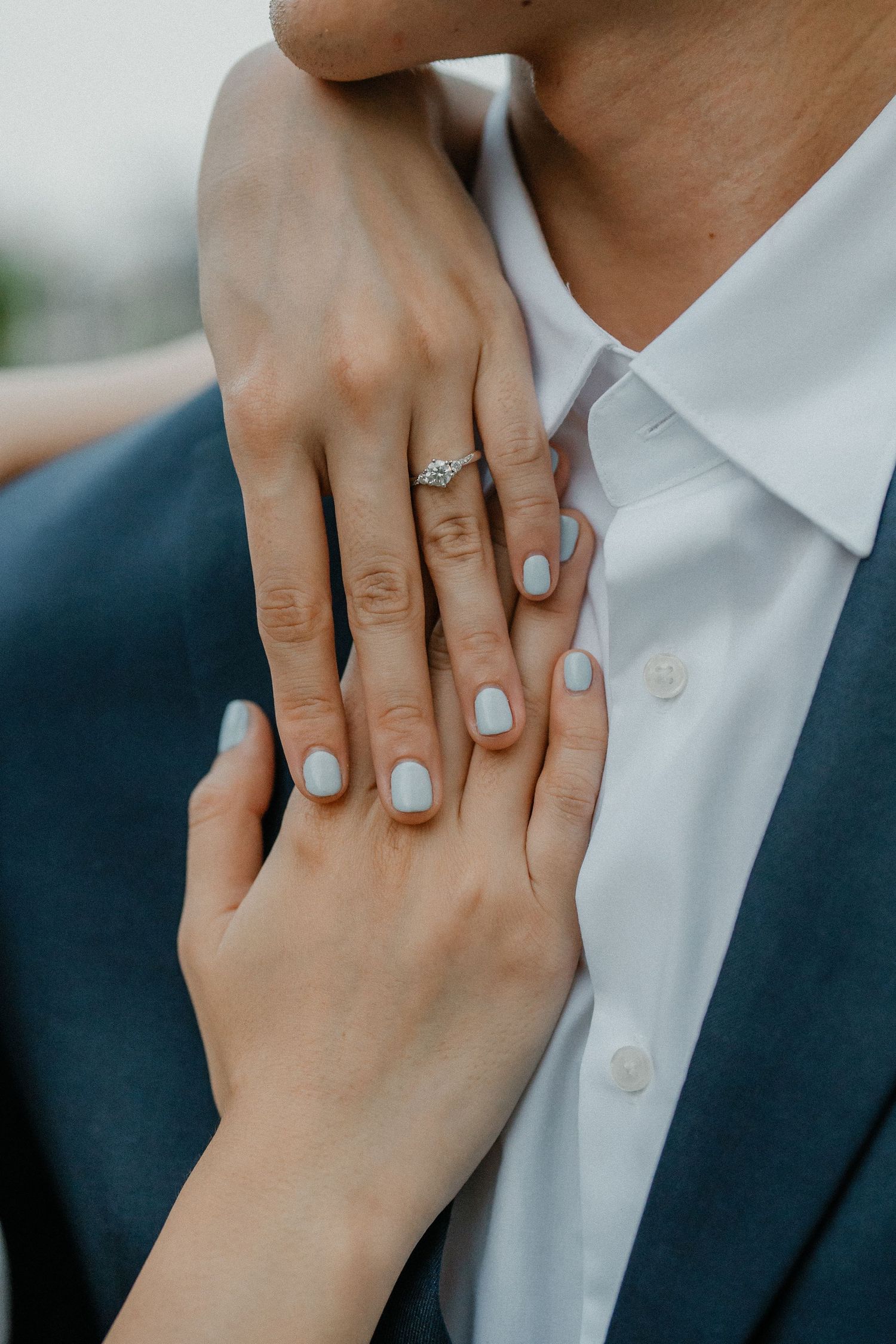 Close-up of hands showing an engagement ring against a white shirt and navy suit.