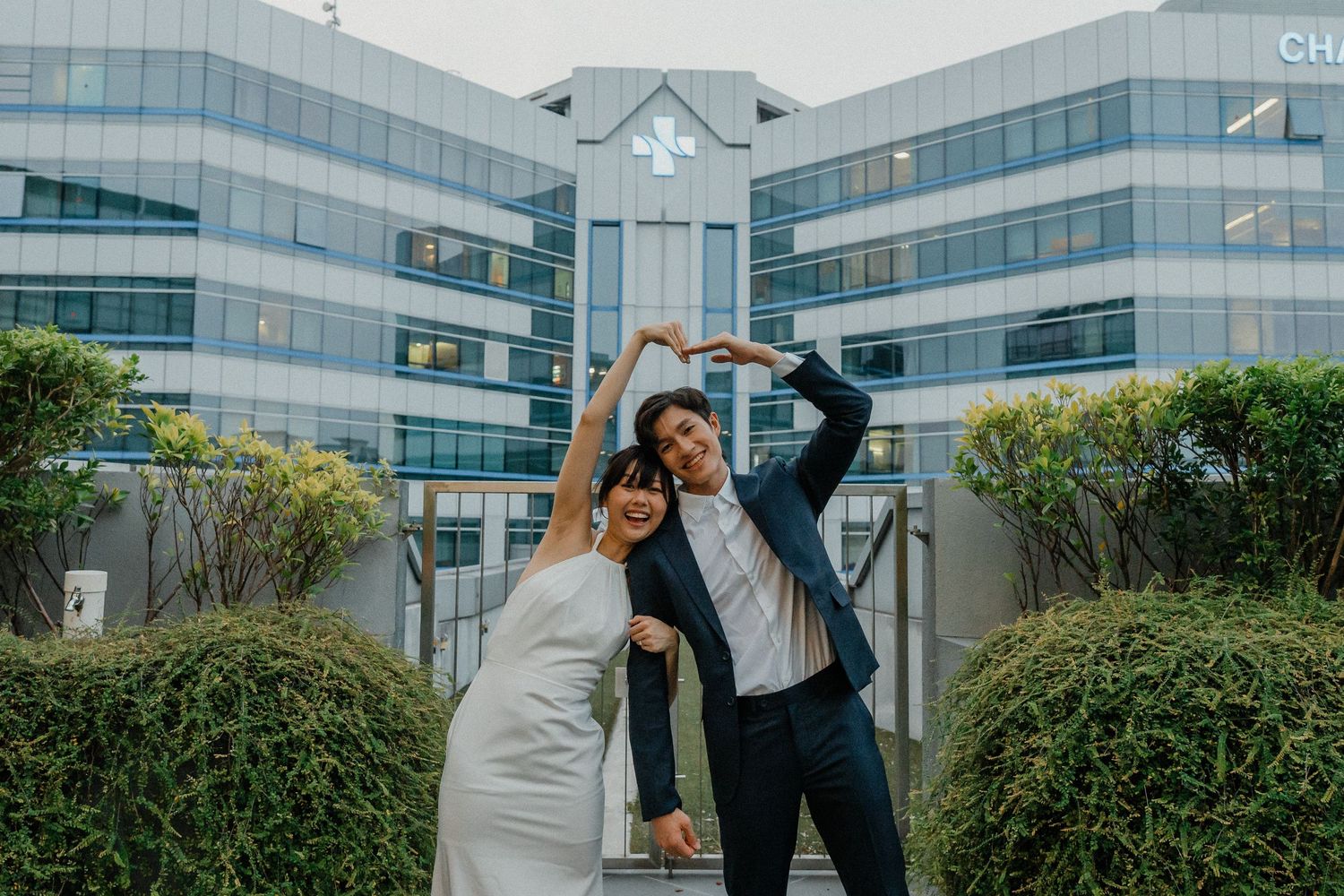 Wedding couple dancing and posing playfully against modern architecture backdrop.
