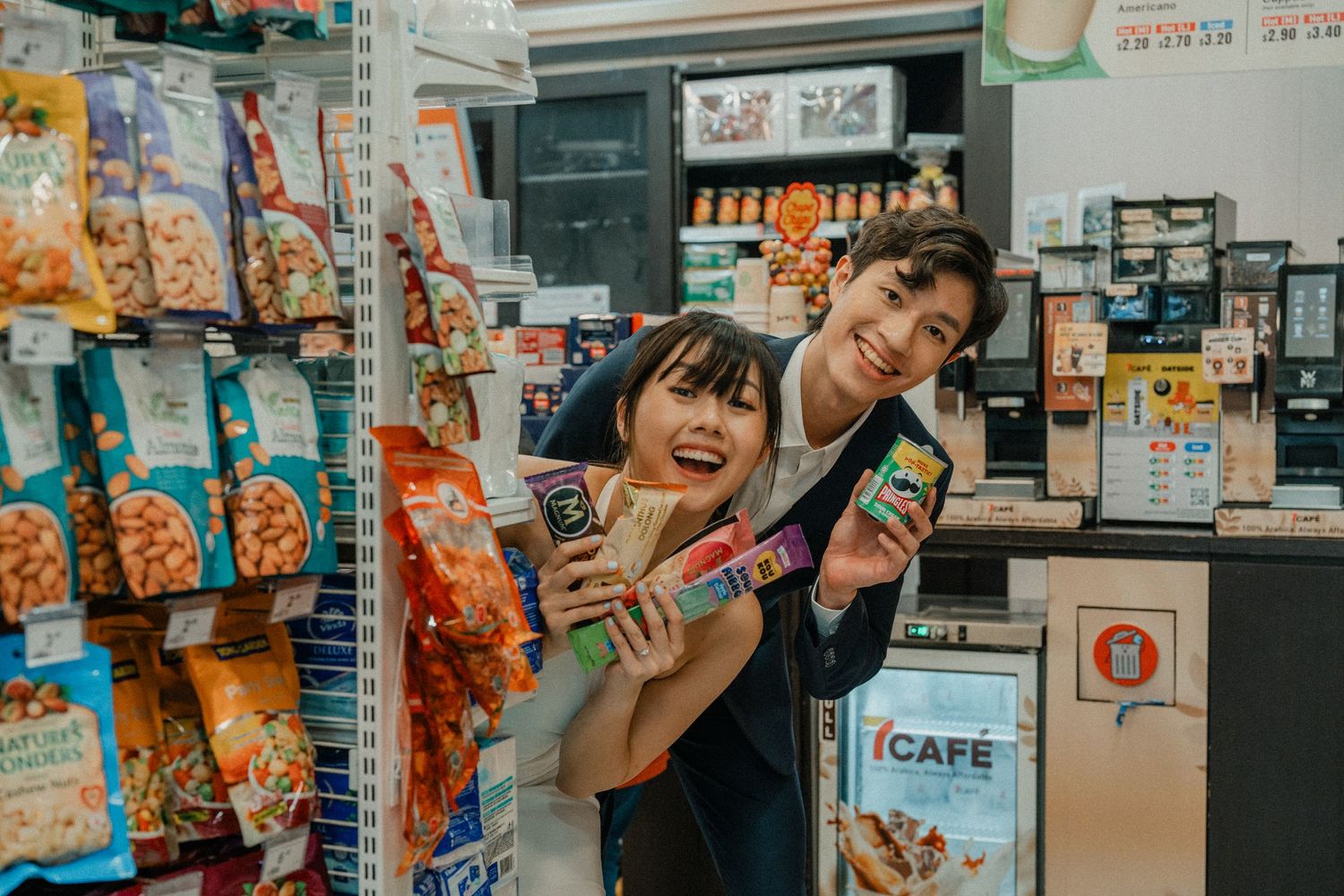 Playful couple having fun shopping in a convenience store aisle filled with snacks.
