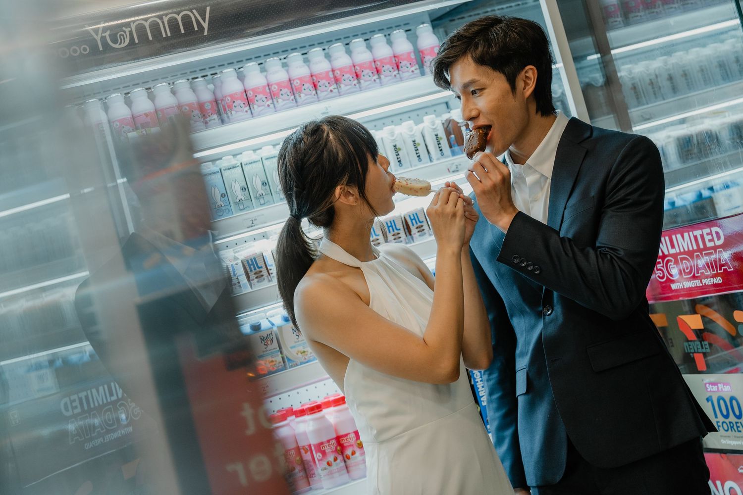 Couple sharing snacks in front of a convenience store cooler.
