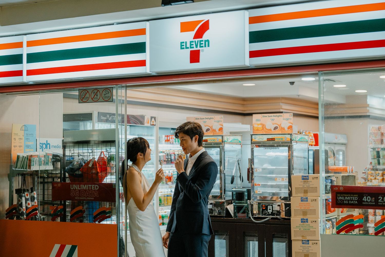 Couple stands outside a 7-Eleven store entrance in formal attire.