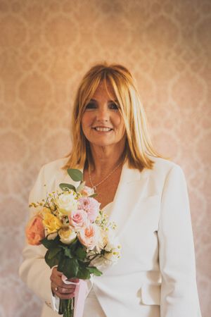 Person in white holding delicate bouquet of pink and yellow roses against textured background.