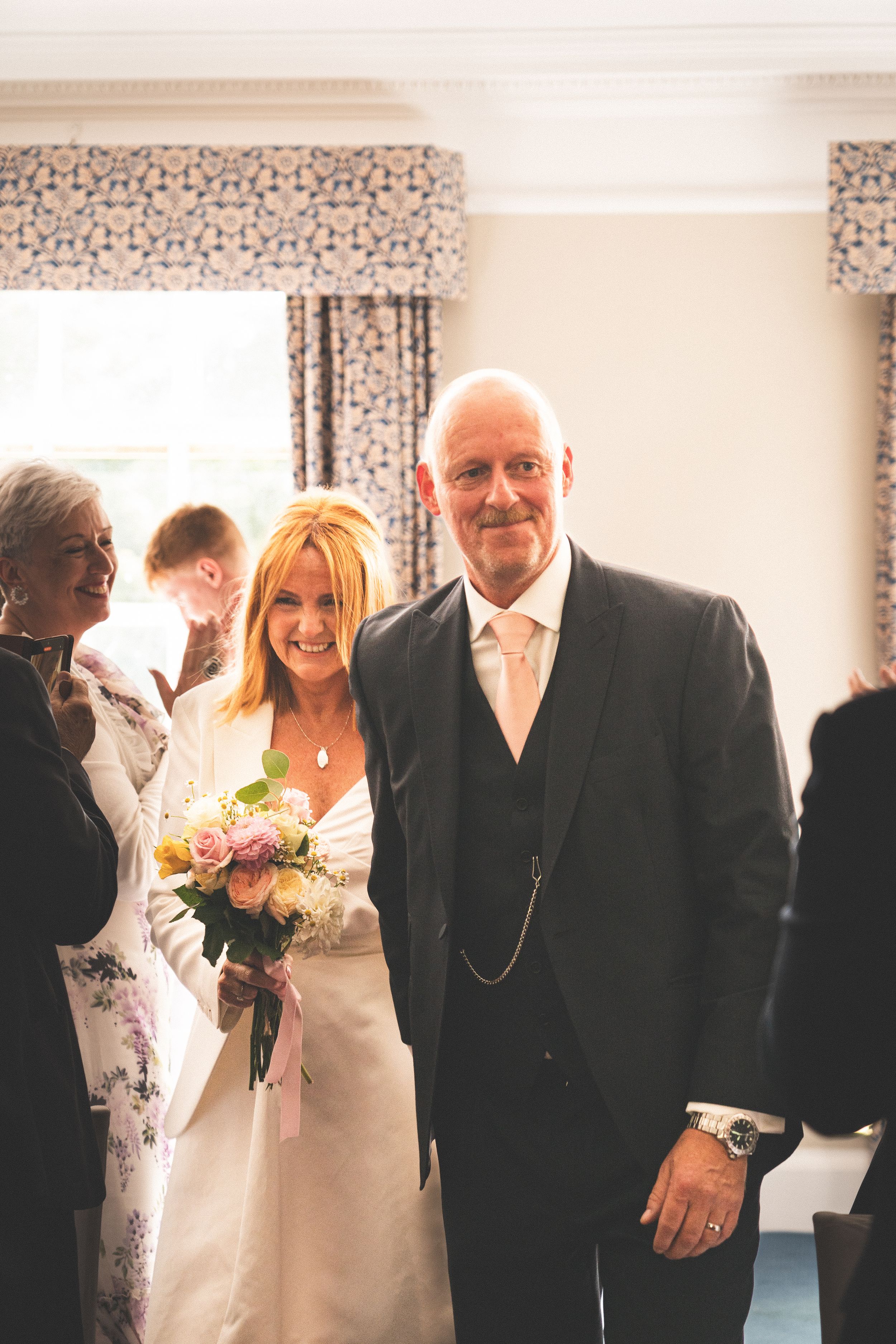 Wedding party gathering in a bright indoor space with patterned curtains.