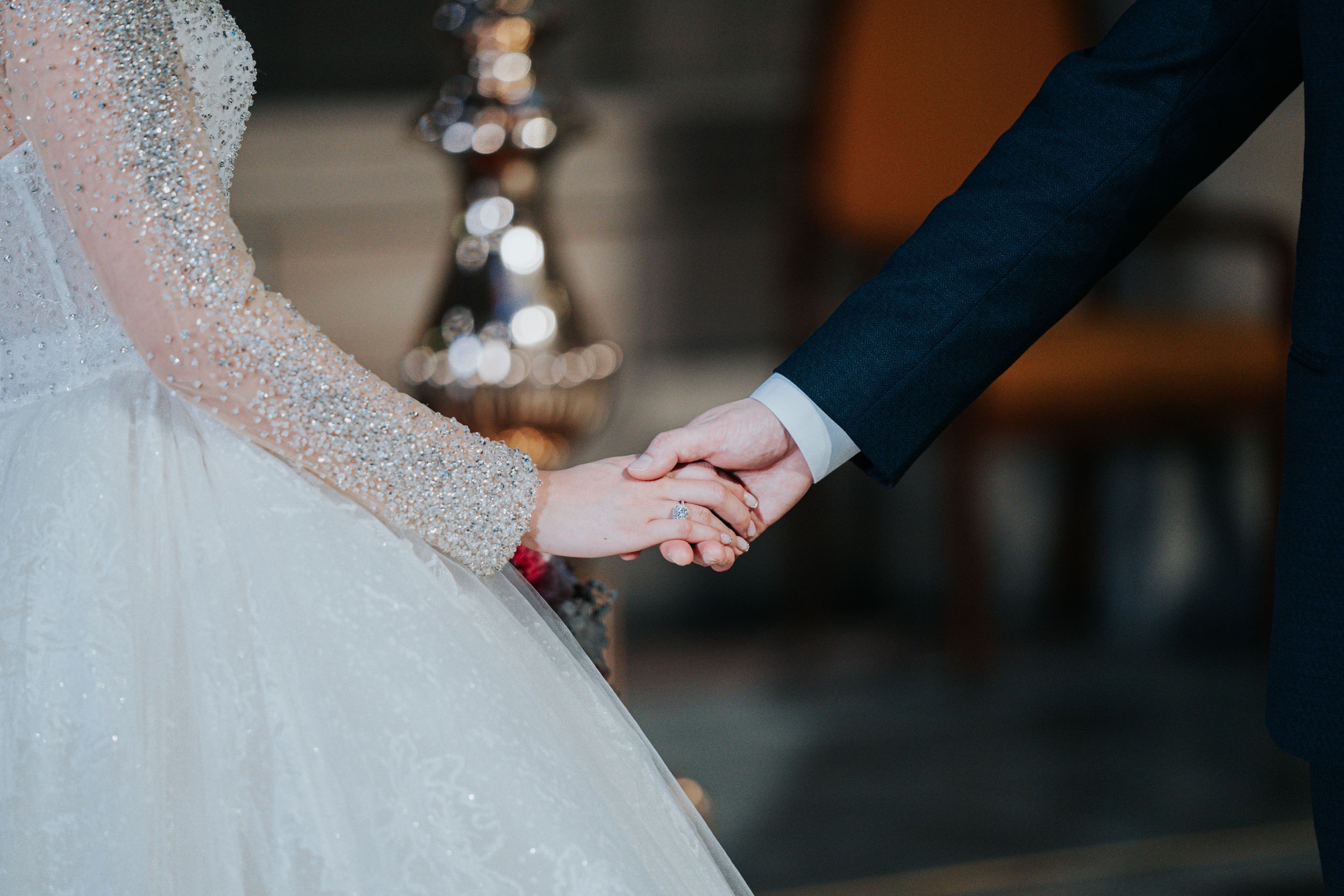 Close-up of bride and groom holding hands showing wedding dress detail and red string.