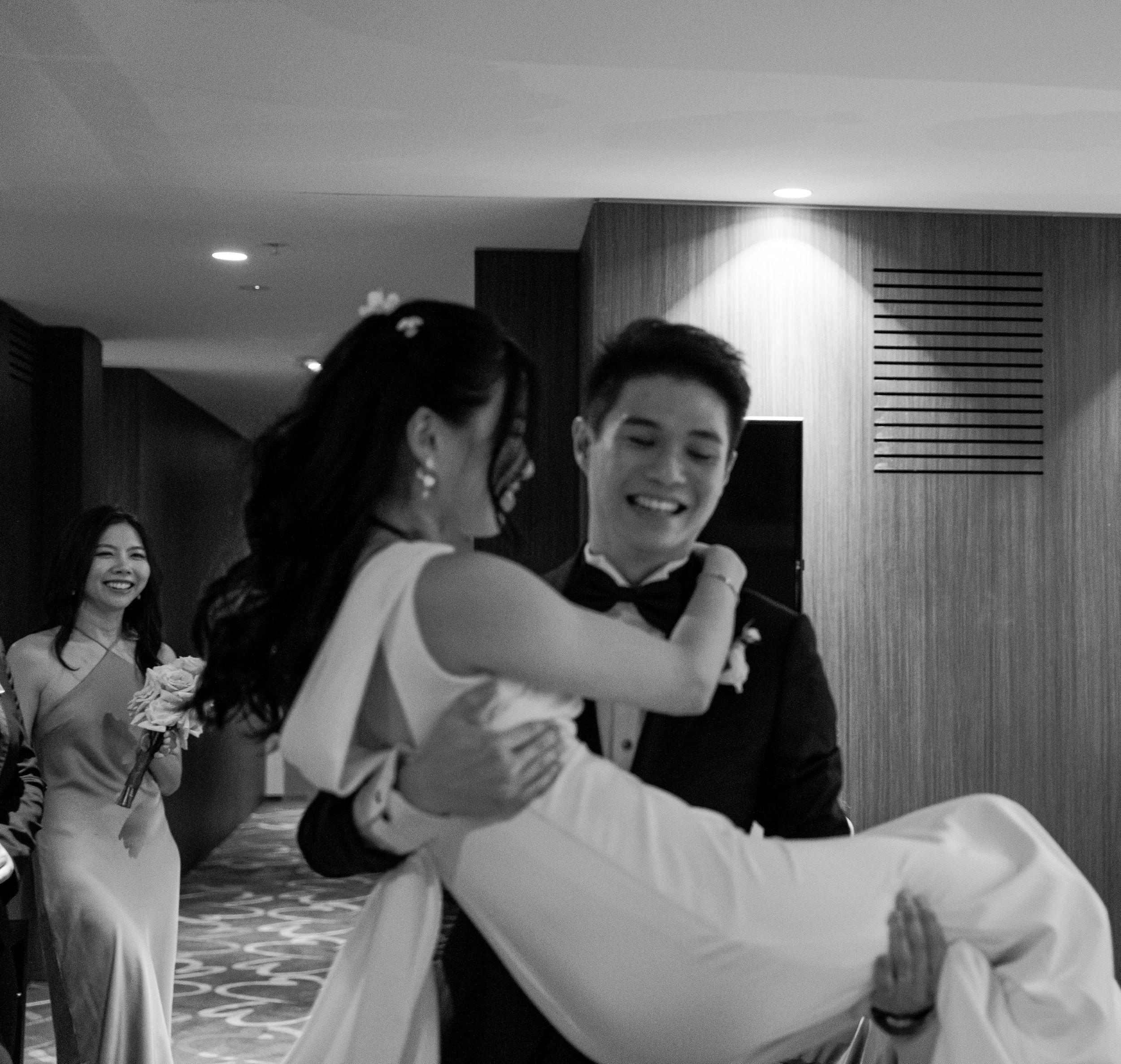 Couple sharing romantic dance moment in black and white with guests looking on.