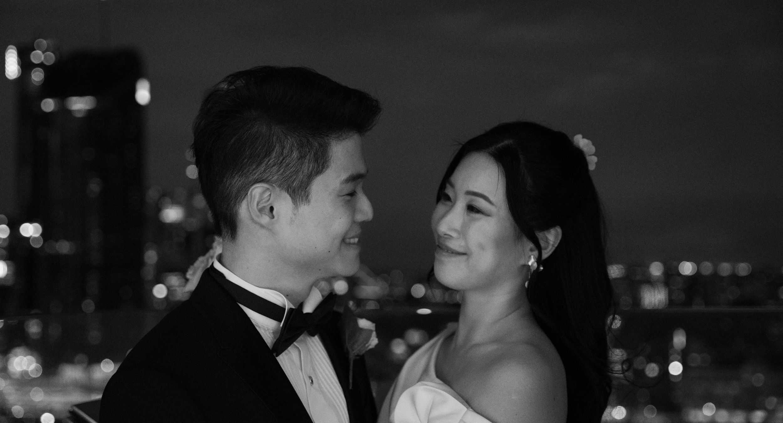 Couple shares intimate moment against city skyline backdrop at night.