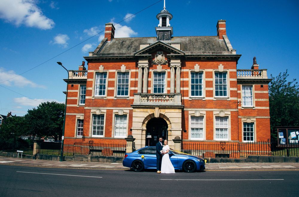 Wedding couple outside historic red brick building under blue sky.