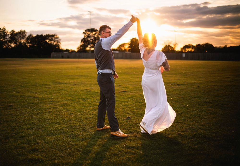 A couple dancing in a golden field during sunset, with the bride's white dress flowing in the warm evening light.