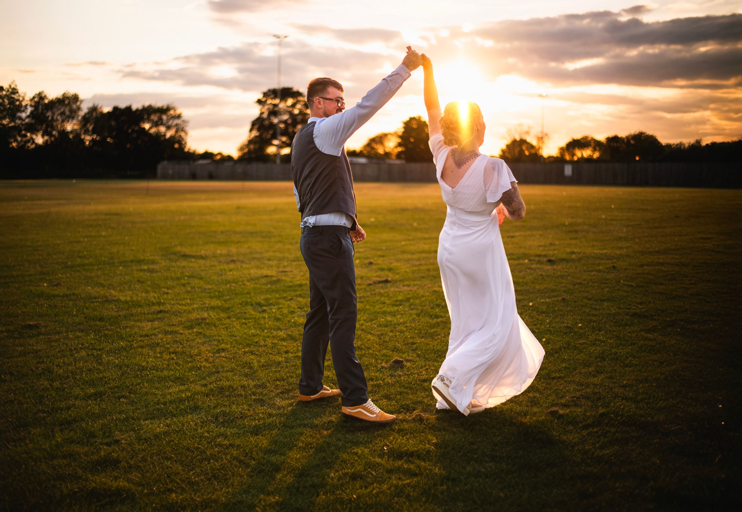 A couple dancing in a golden field during sunset, with the bride's white dress flowing in the warm evening light.