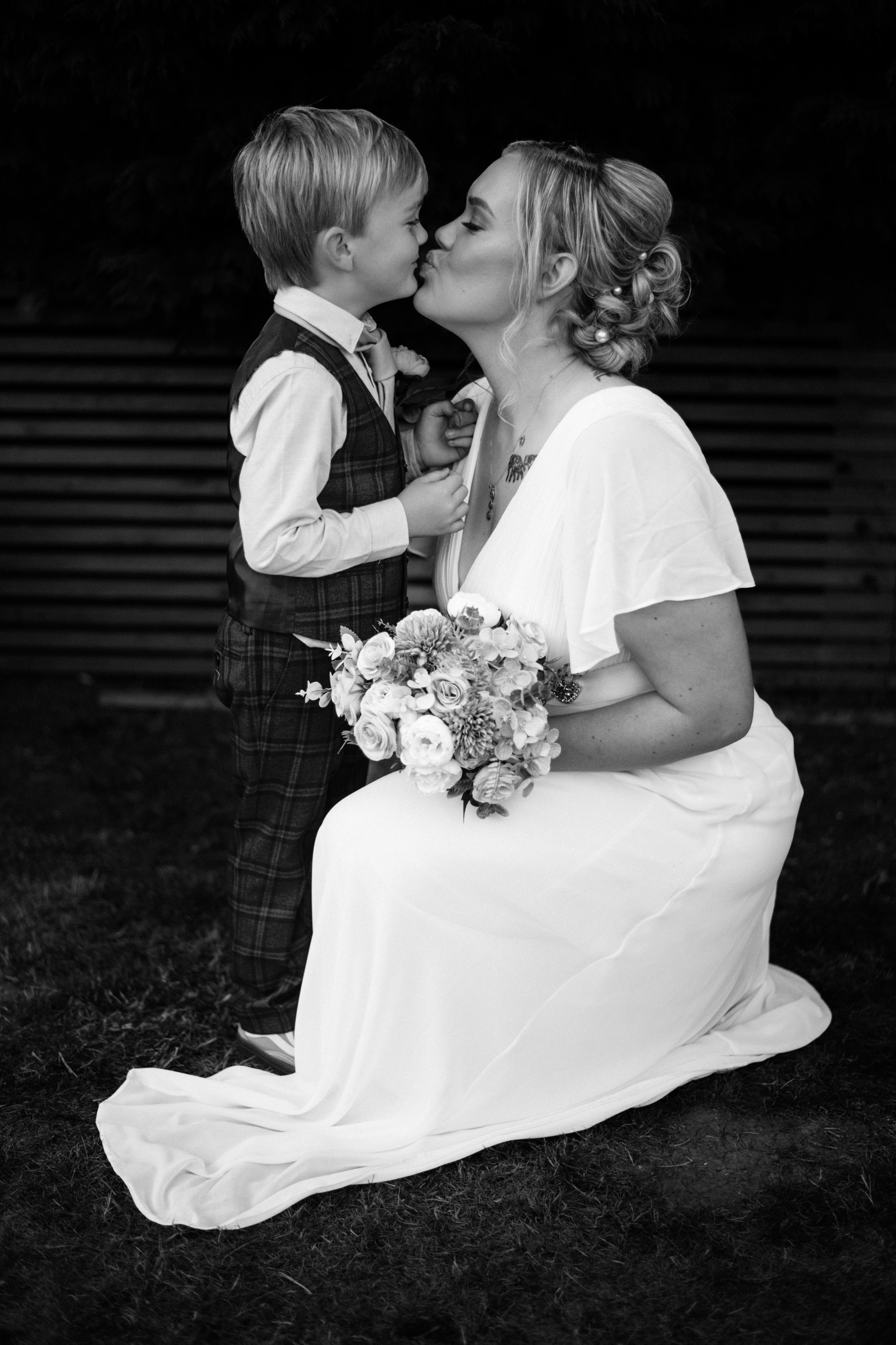 A touching black and white portrait of a bride sharing a special moment with a young child in formal attire.