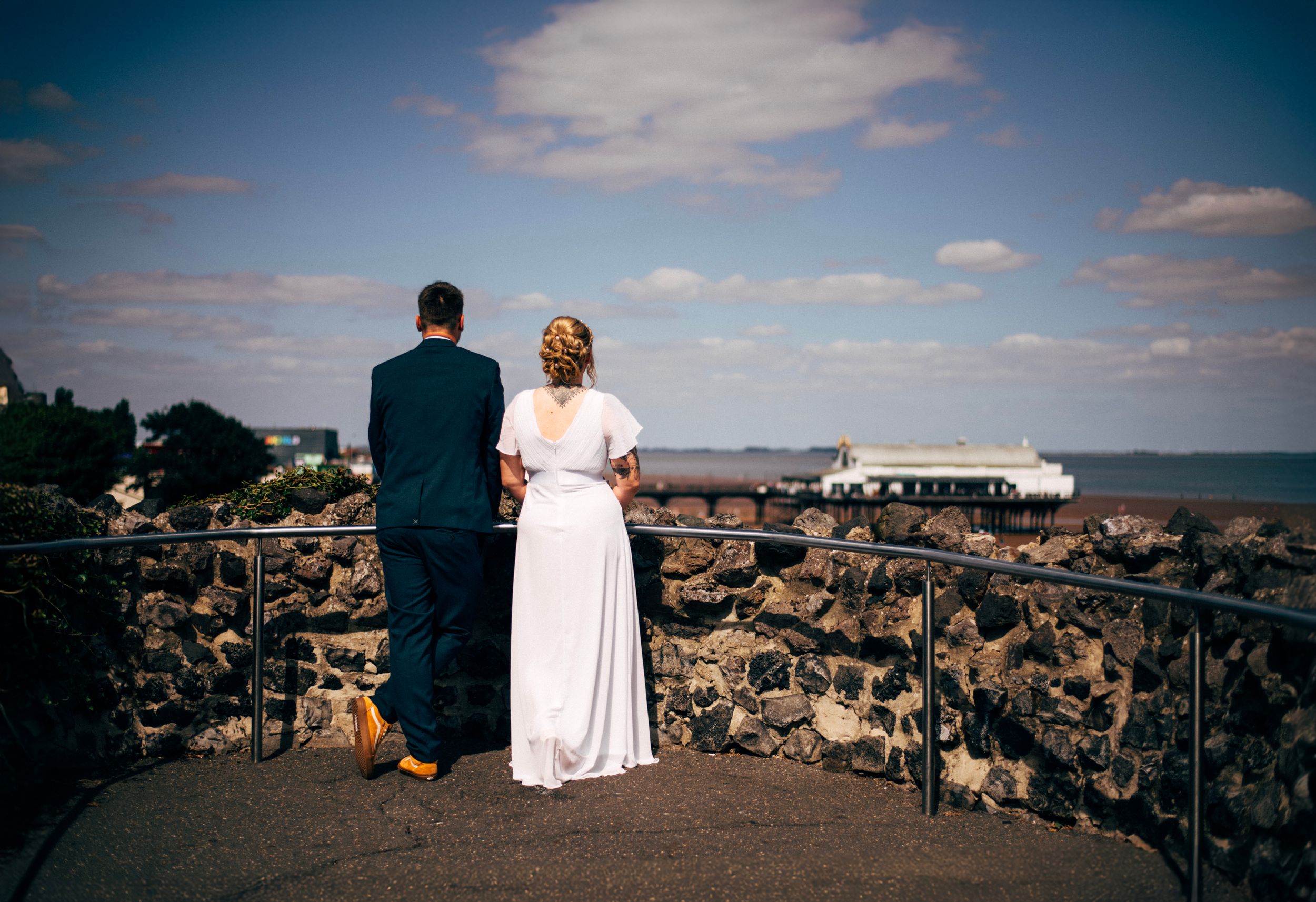 A couple in wedding attire enjoying a scenic overlook while standing on stone walls.