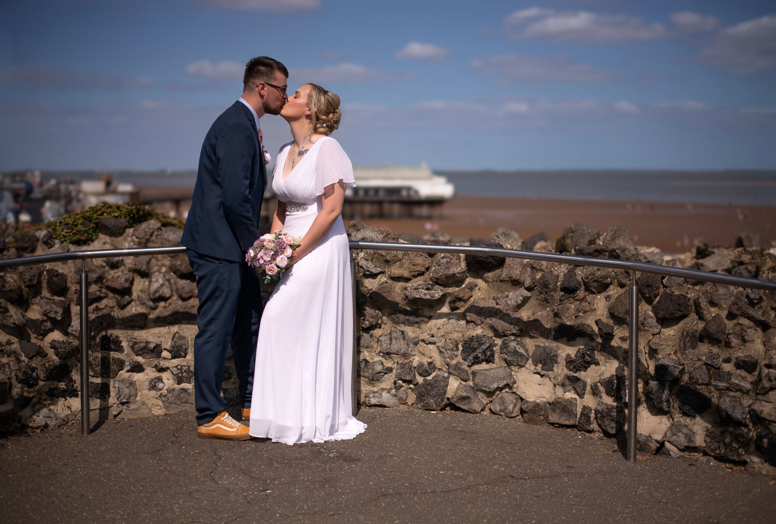 A couple sharing an intimate moment on a stone overlook with ocean views in the background.