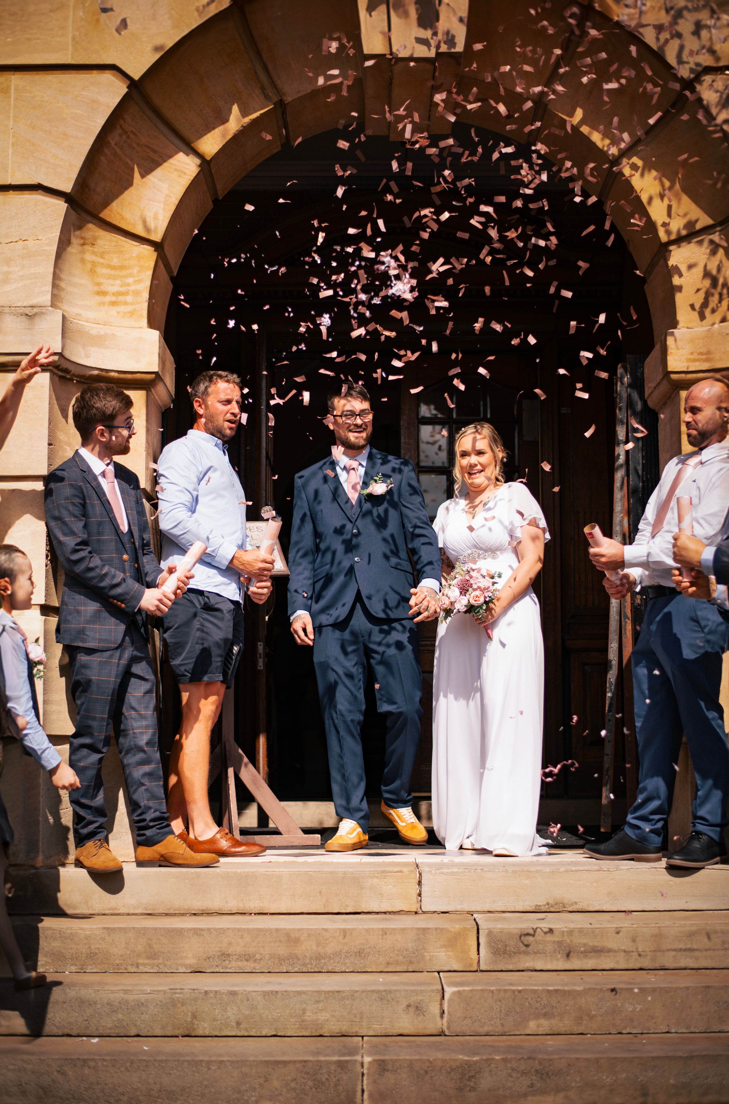Wedding party celebrates on church steps as confetti falls around the newlyweds.