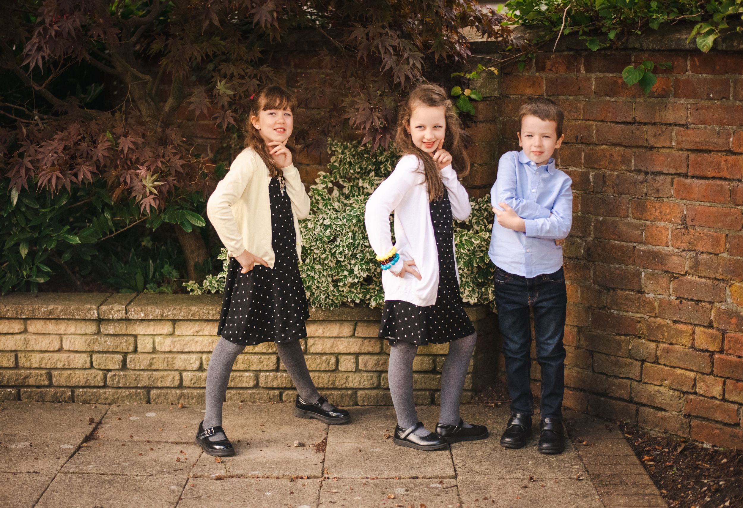 Three children posing playfully against a brick wall in formal attire.