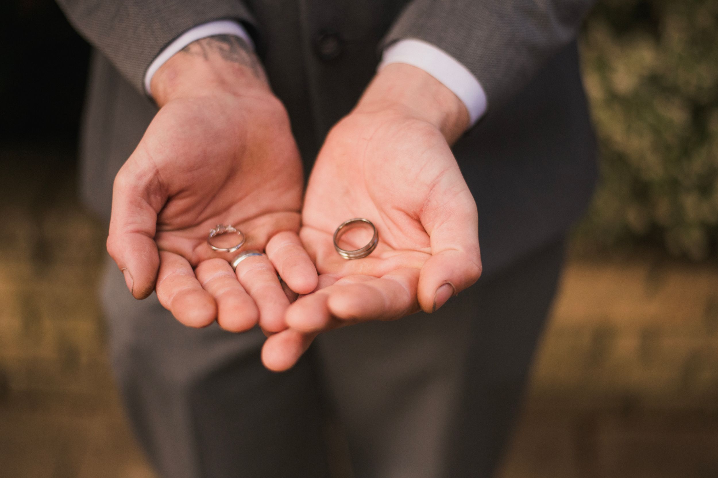 Two hands hold wedding rings against a neutral background.