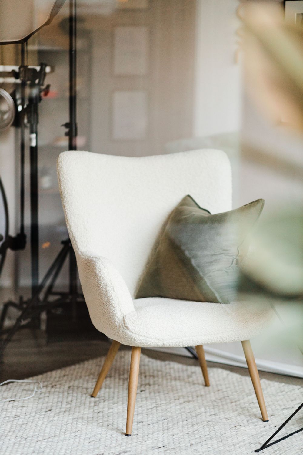 White boucle accent chair with gray pillow on area rug in minimalist interior setting.