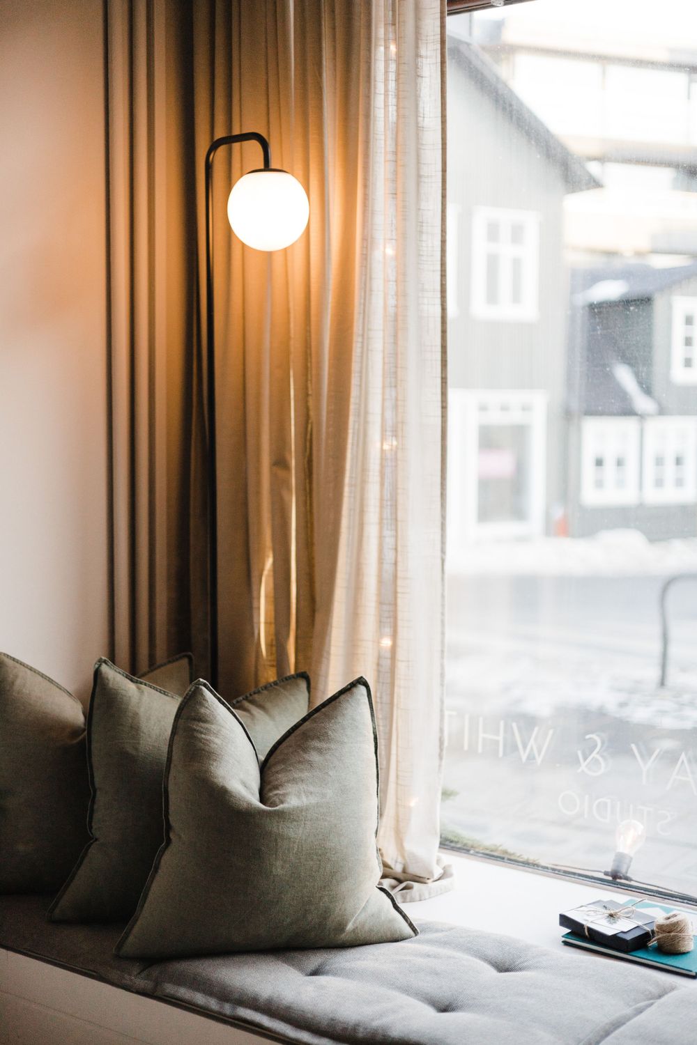 Modern living room corner with globe lamp, gray throw pillows and sheer curtains by window.