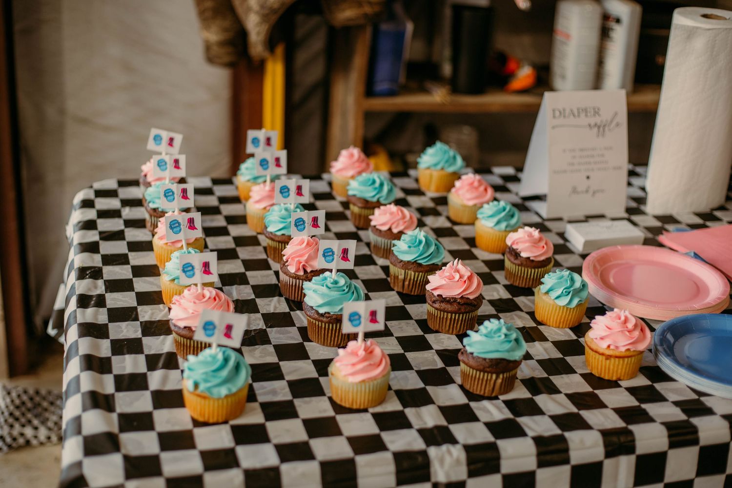 Colorful cupcakes with blue and pink frosting displayed on black and white checkered tablecloth.