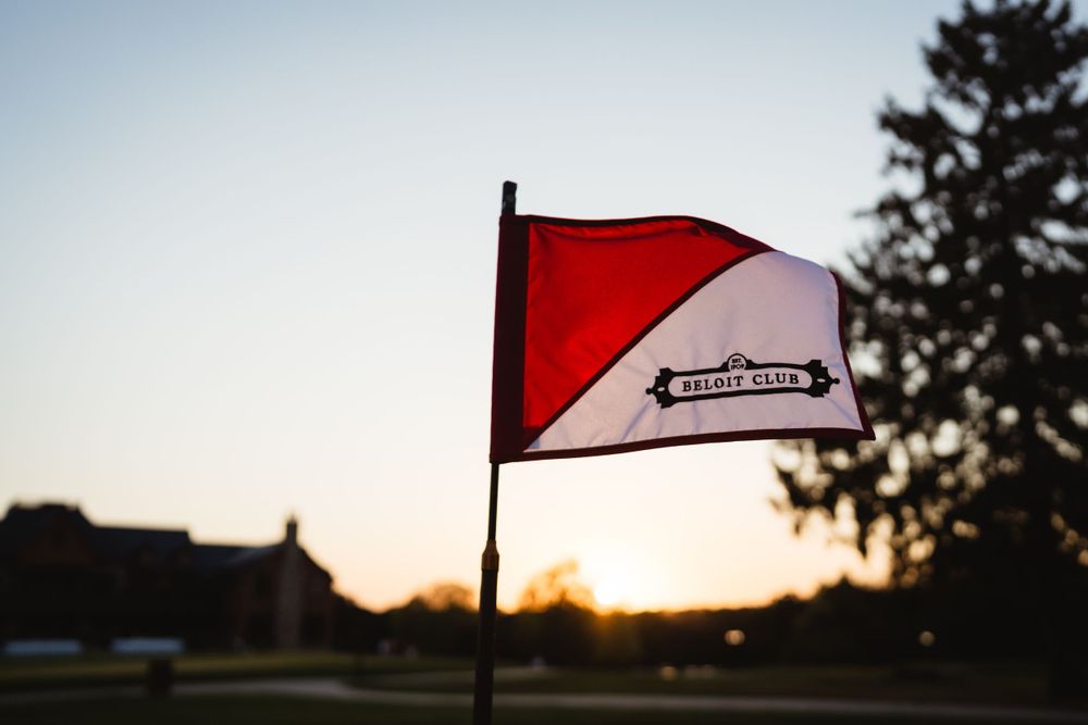 Red and white flag waves against a sunset sky at a golf course.