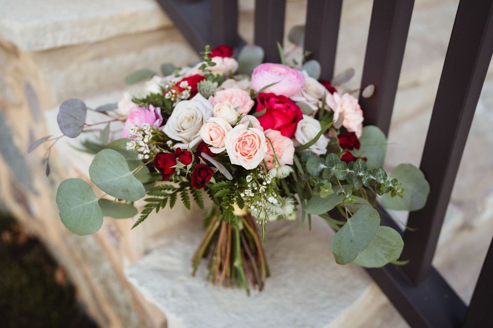 Beautiful wedding bouquet with pink and red roses accented with eucalyptus leaves rests on a dark railing.