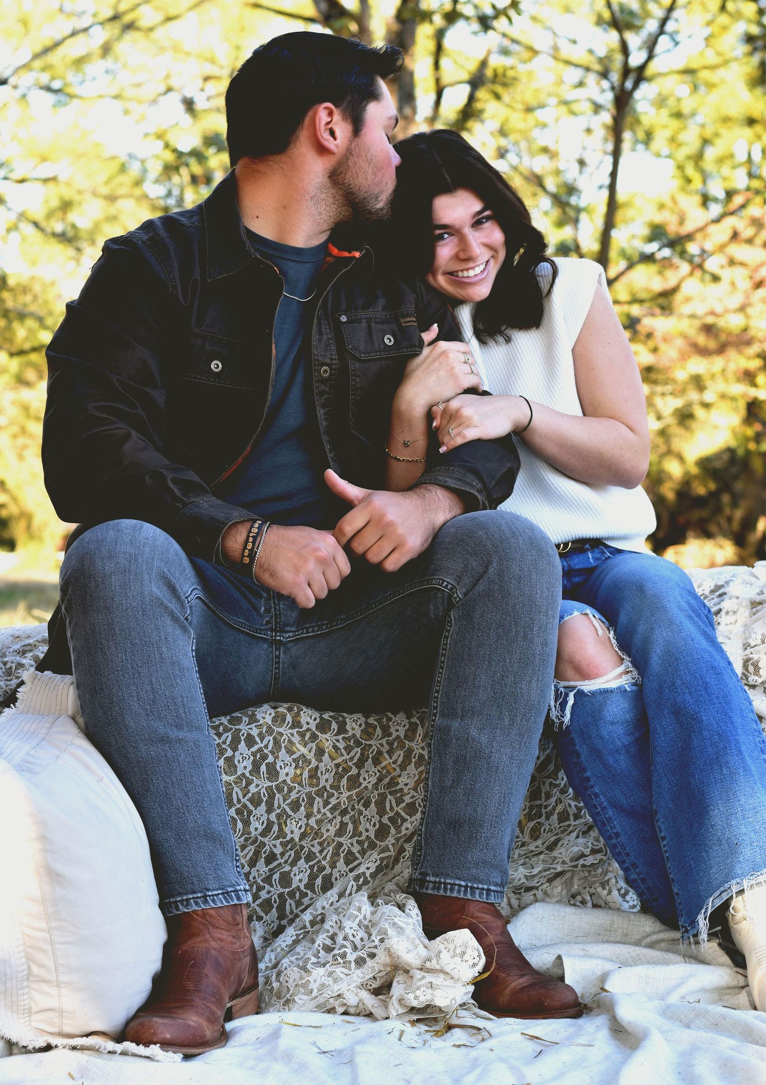 A couple sits together on a blanket outdoors during a sunny autumn day.