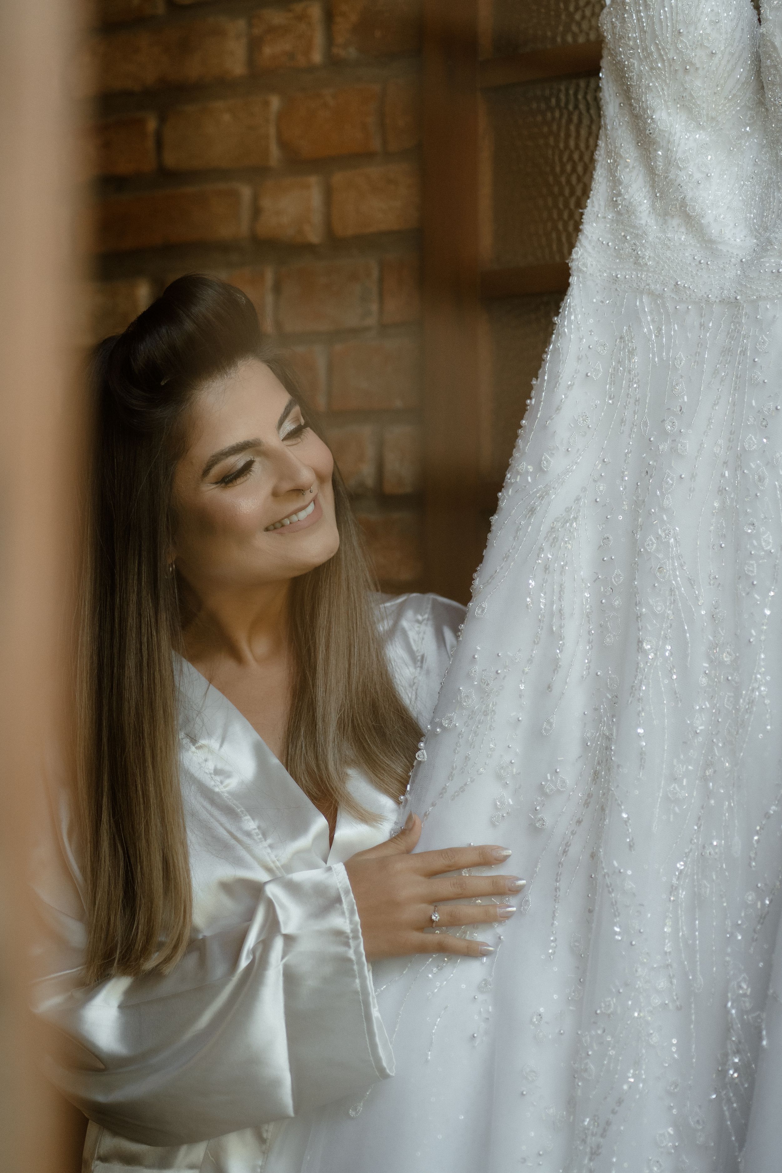 A white silk robe contrasts beautifully with a sequined wedding gown hanging against exposed brick.