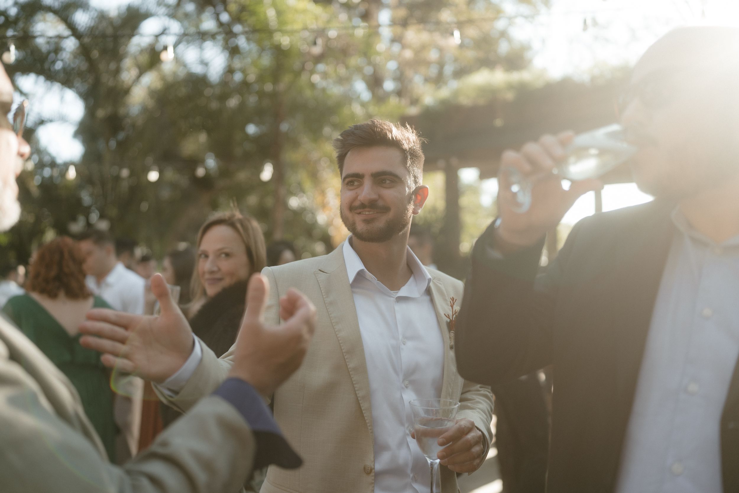 Guests enjoying cocktails and conversation at an outdoor wedding reception in golden sunlight.