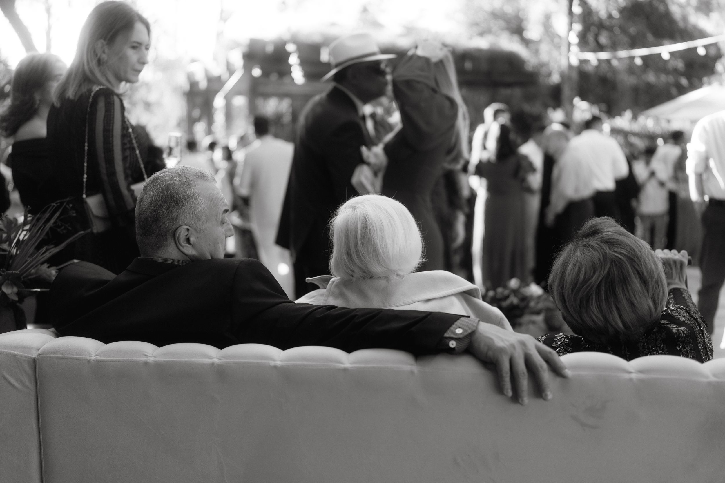 Black and white image of guests relaxing on an outdoor couch during a social gathering.