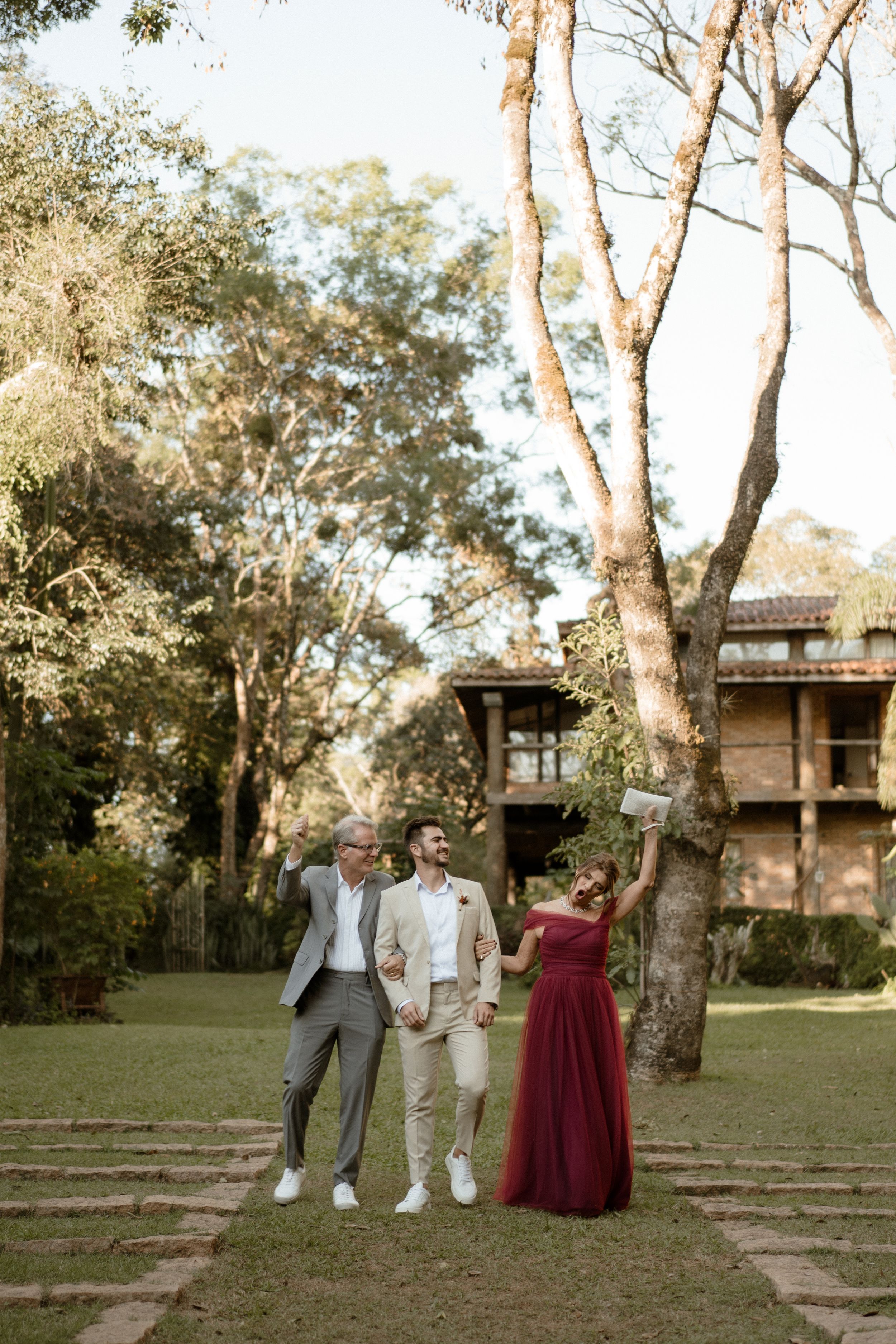 Wedding party posed in front of a rustic wooden building surrounded by tall trees.