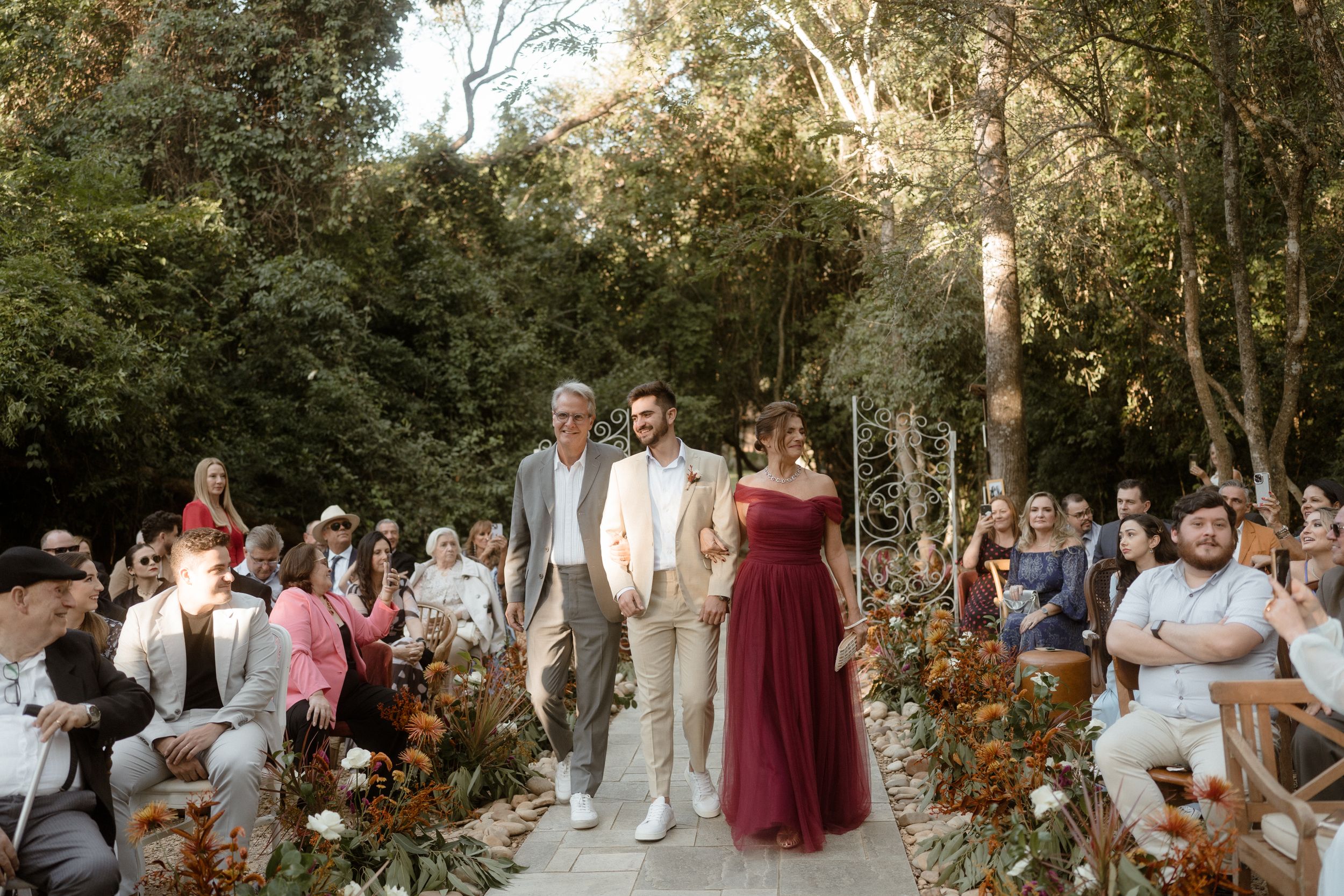 Outdoor wedding ceremony setup with floral decorations and guests seated in a garden setting.