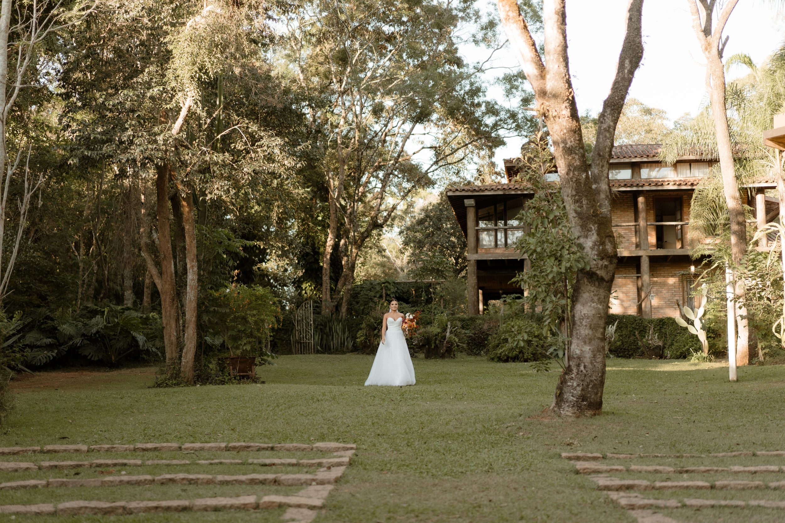 Bride in white dress walking across lawn towards rustic treehouse-style building.