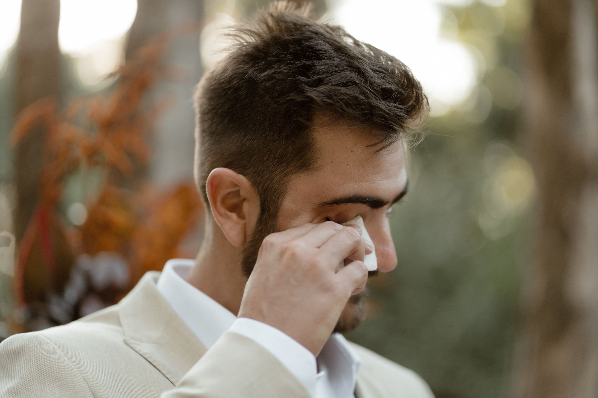 Emotional moment captured during outdoor wedding as groom wipes tears.