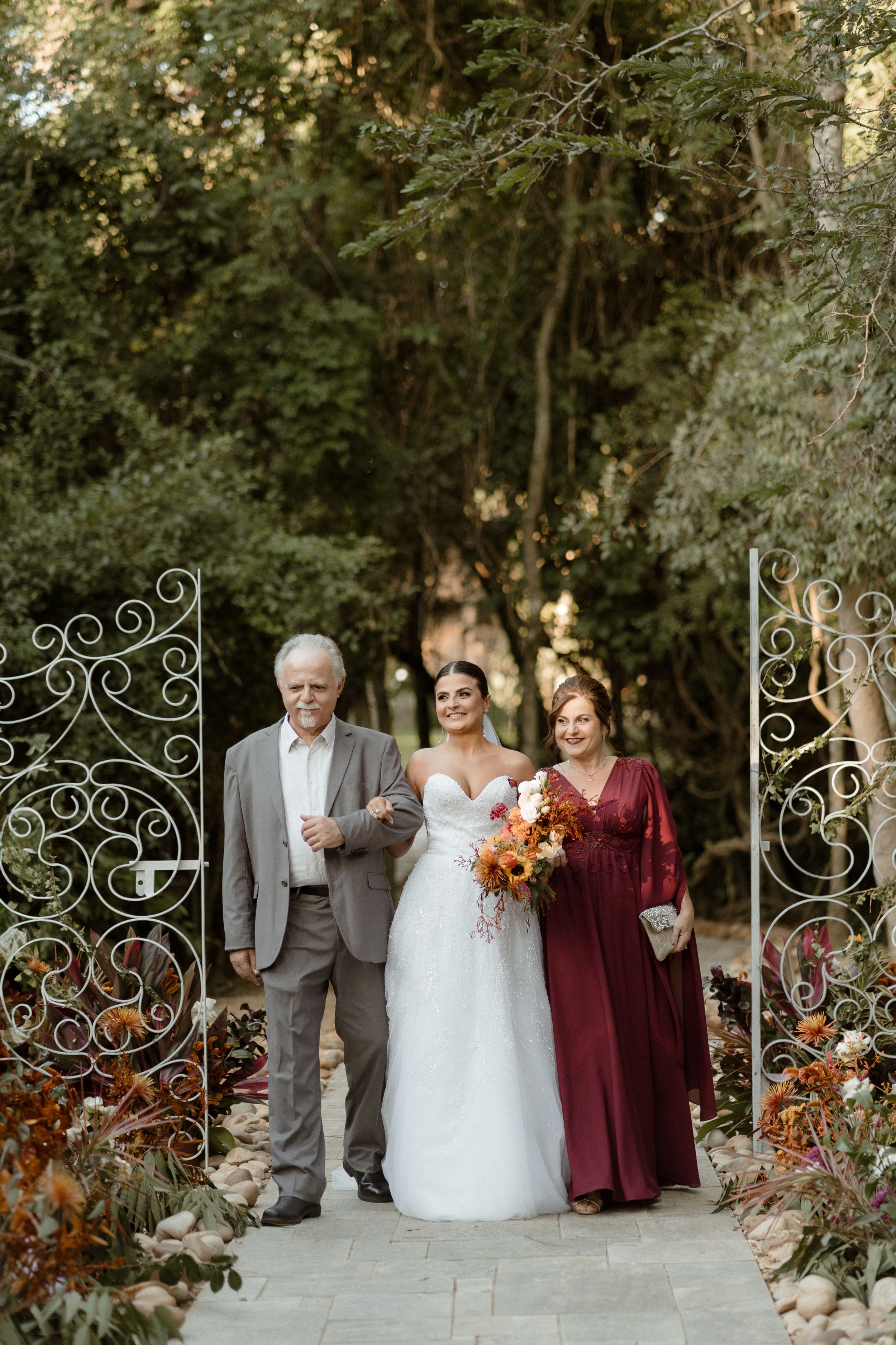 Bride walking through ornate garden gates with bouquet and wedding party members.